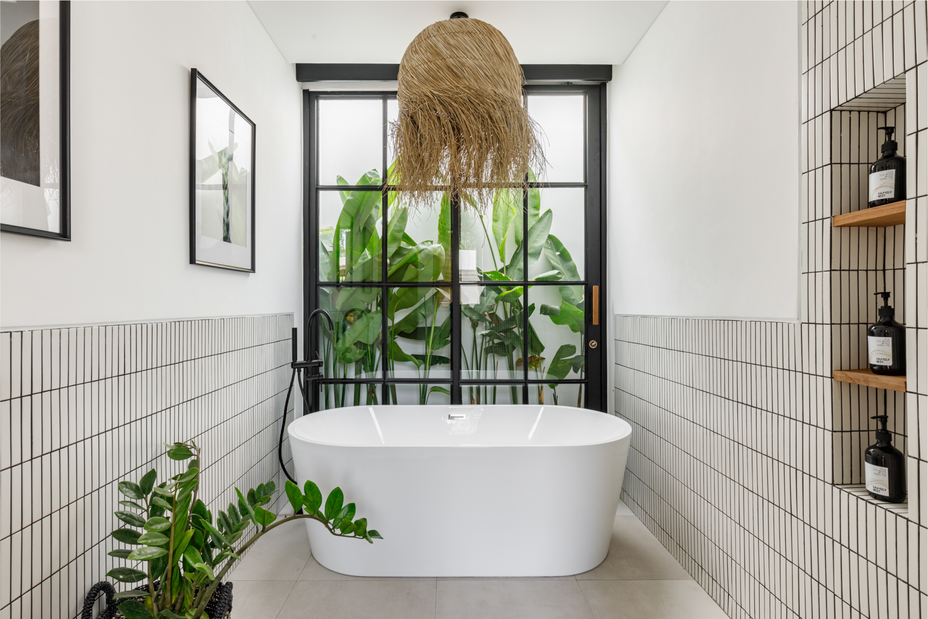 Modern bathroom with freestanding tub, tiled walls, and large window with plants