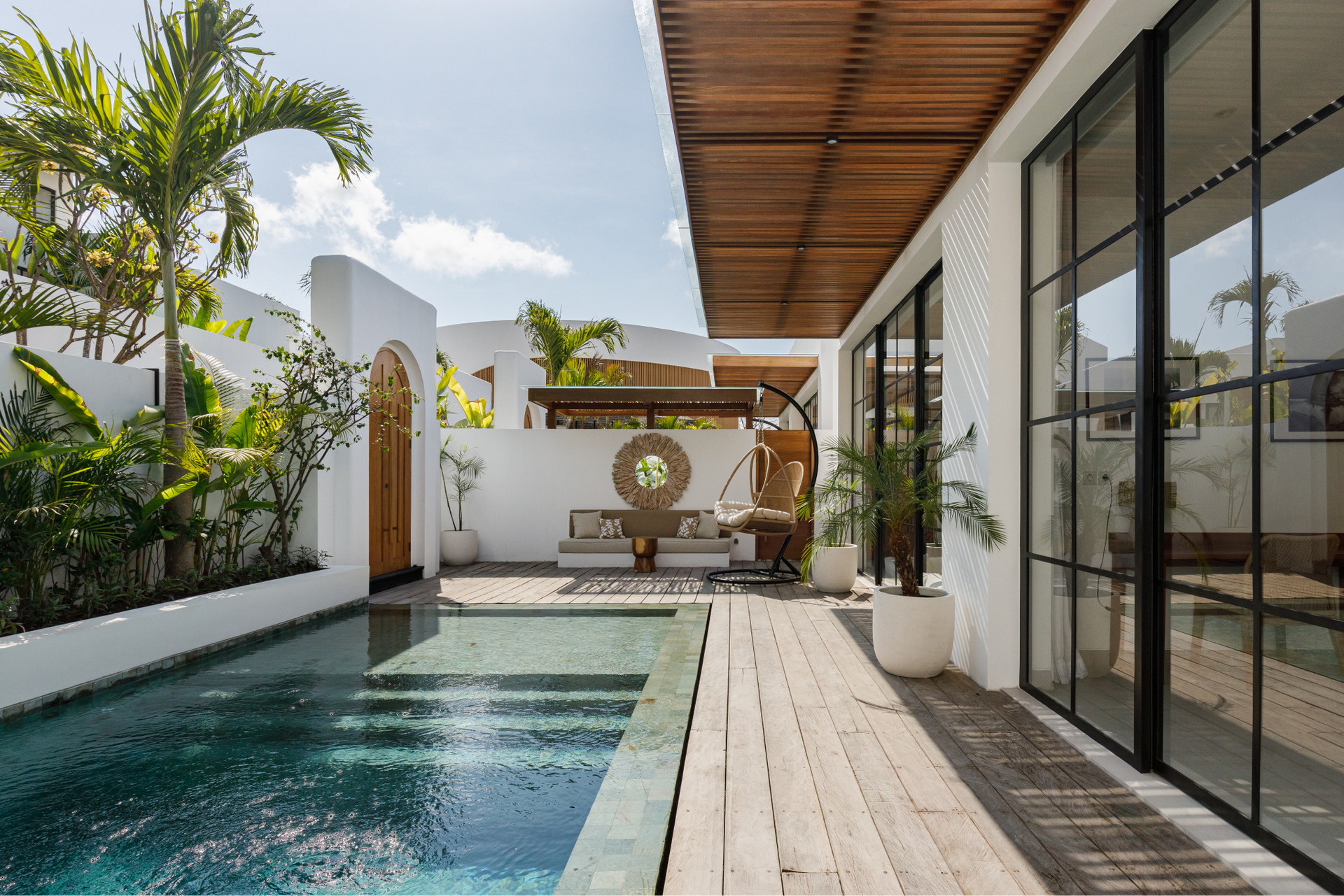 Modern villa courtyard with a swimming pool, wooden deck, and glass sliding doors under a pergola