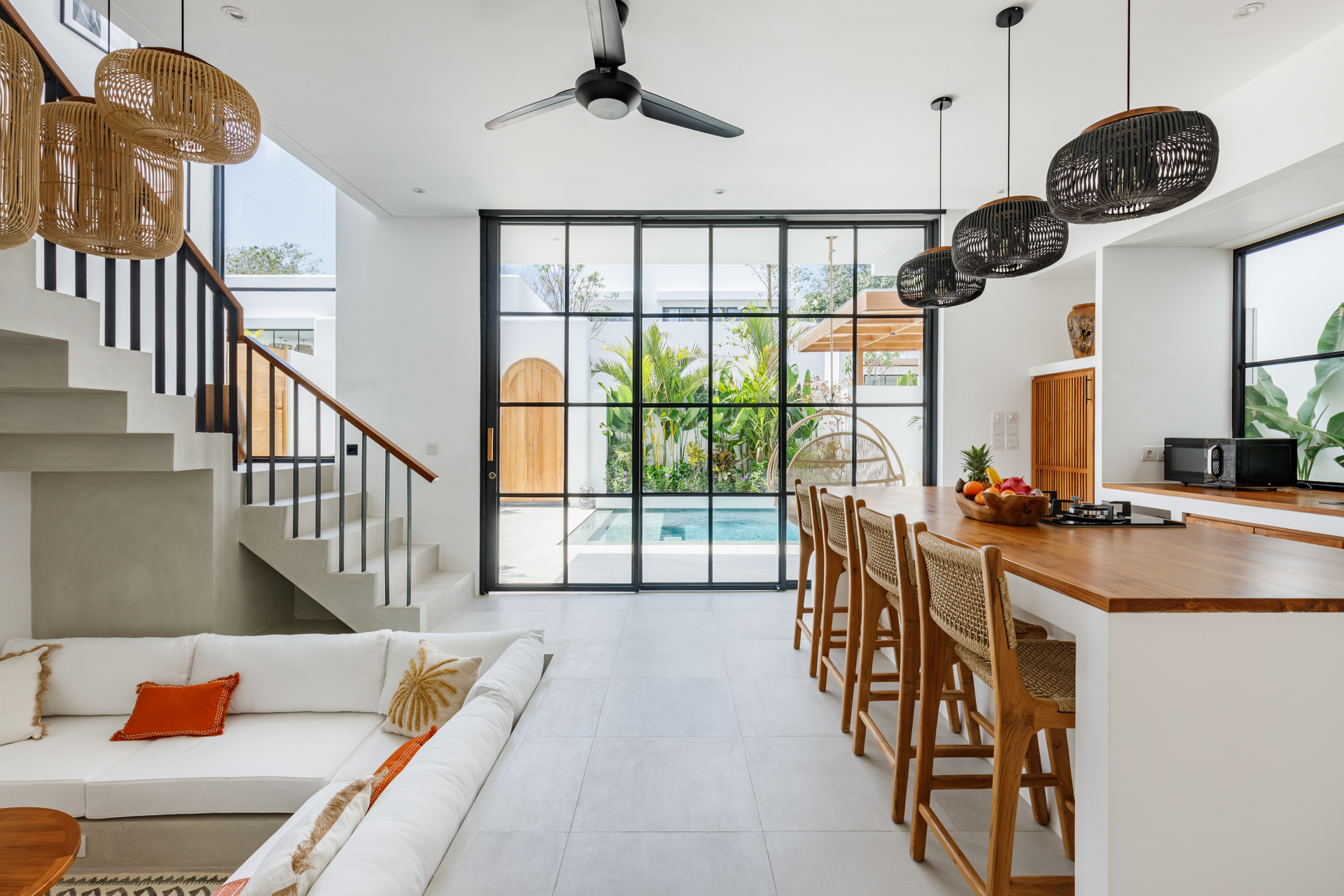 Bright open living room with staircase, kitchen island, and large sliding glass doors leading to a patio.