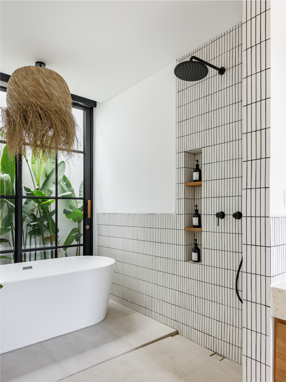 Modern bathroom with freestanding tub, black shower fixtures, and white tile walls by a large window