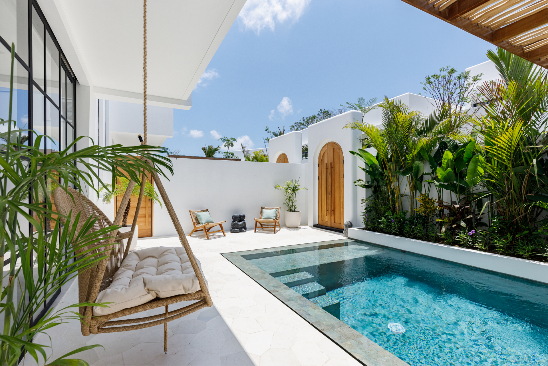 Bright tropical patio with a blue swimming pool, white walls, and a wooden swing chair