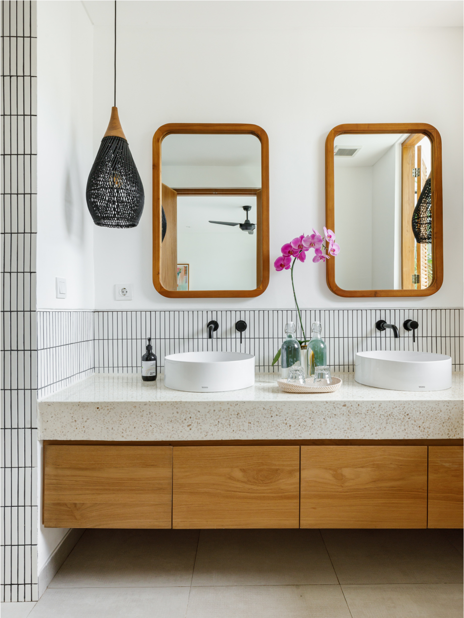 Modern double-sink bathroom vanity with wood cabinets, white tile walls, and two framed mirrors with a purple orchid.