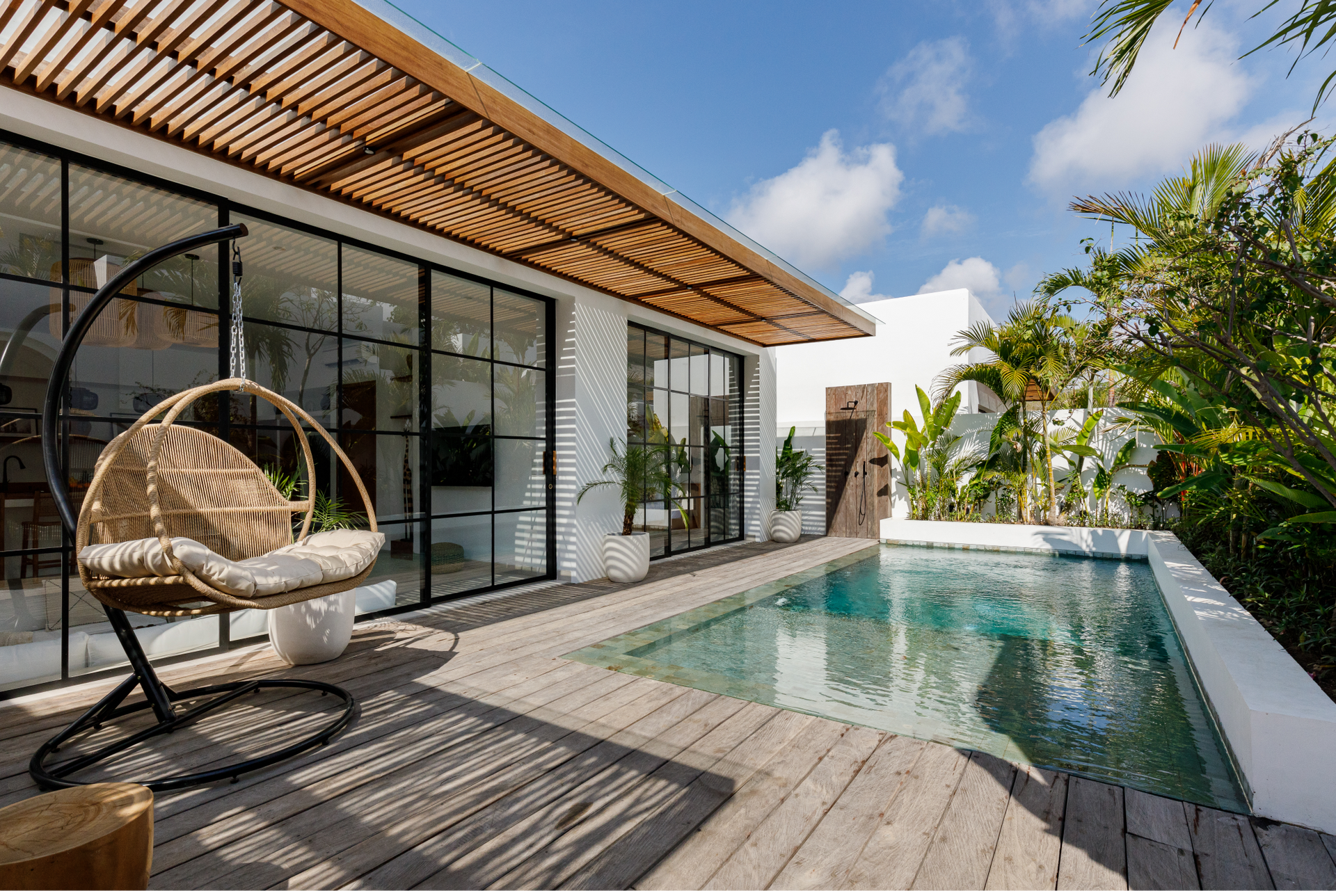 Modern villa patio with a pool, wicker lounge chair, and sliding glass doors under a wooden pergola