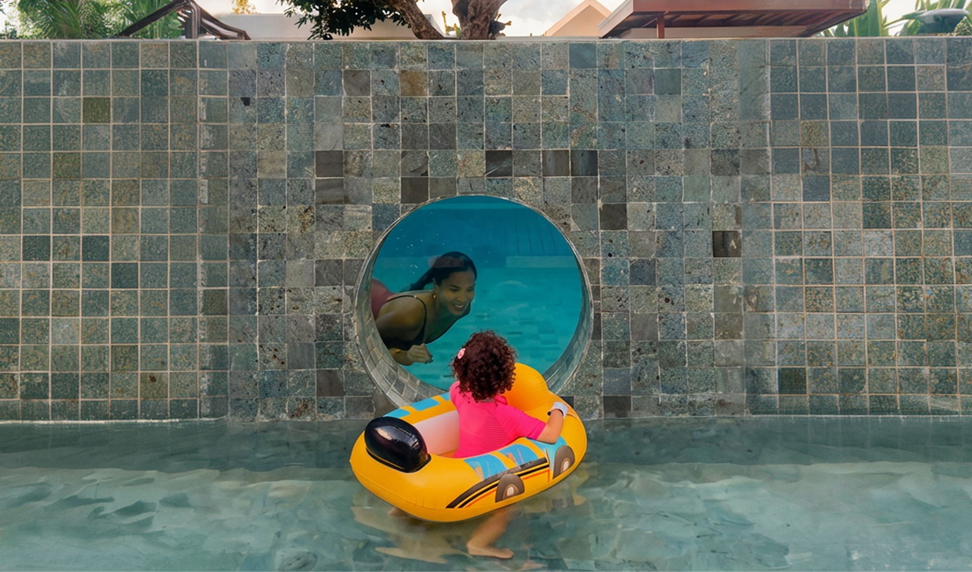 Child in an orange float facing a circular wall opening with a bird perched inside, in a pool.