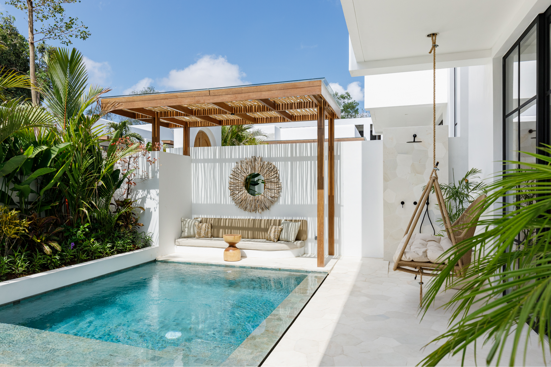 Modern patio with a small turquoise pool, white lounge bench, and wooden pergola beside a white house
