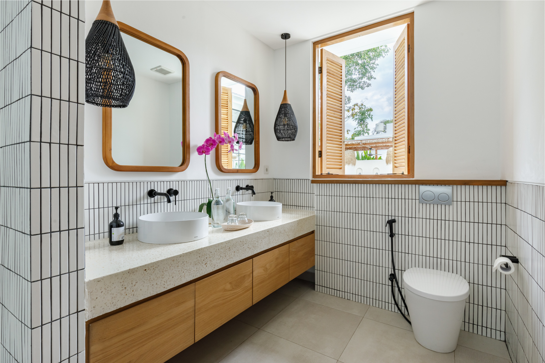 Modern bathroom with white tile walls, wooden vanity, round mirror, and window view outdoors