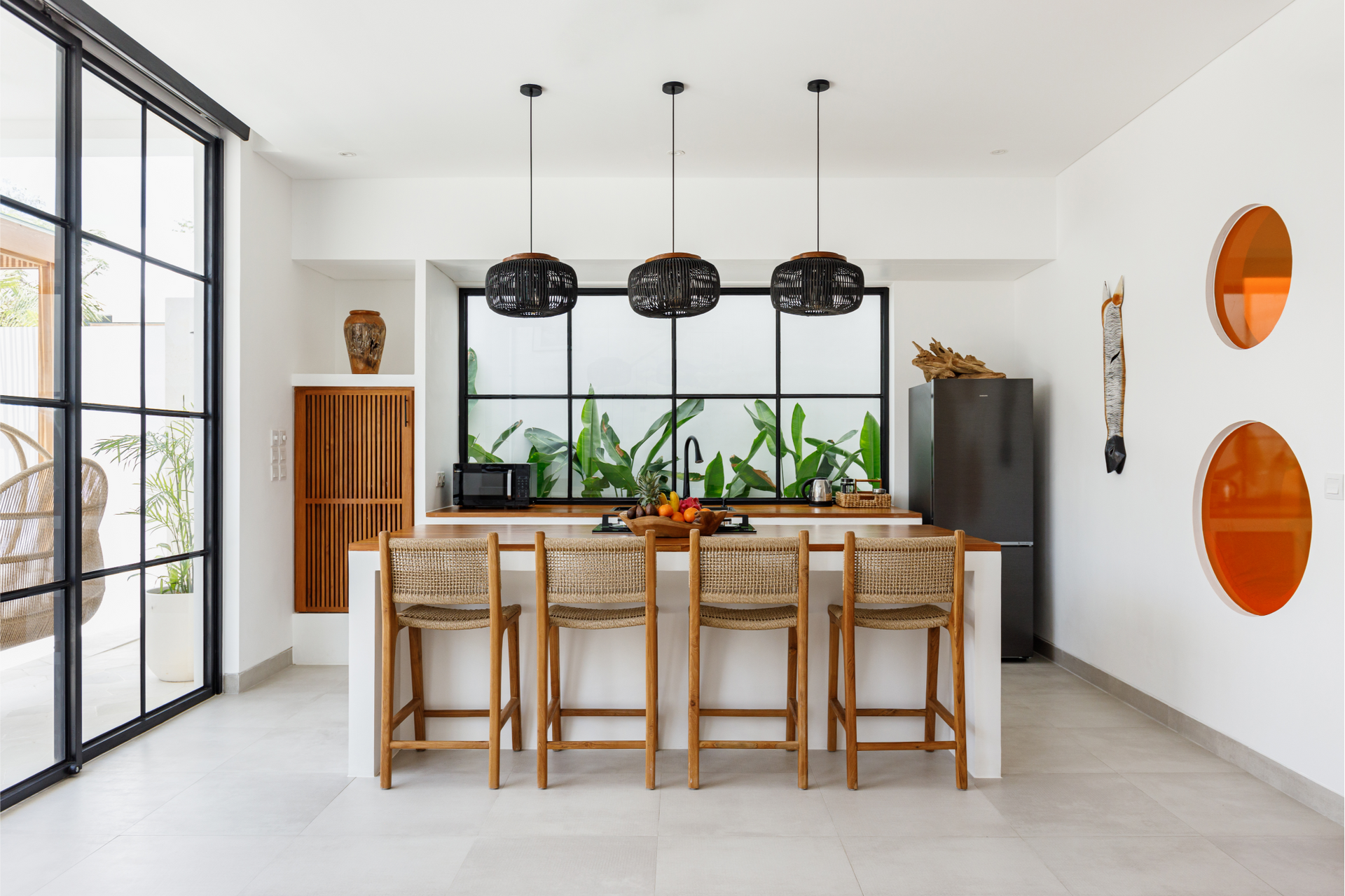 Bright modern dining room with bamboo chairs, pendant lights, and a glass wall by indoor plants.