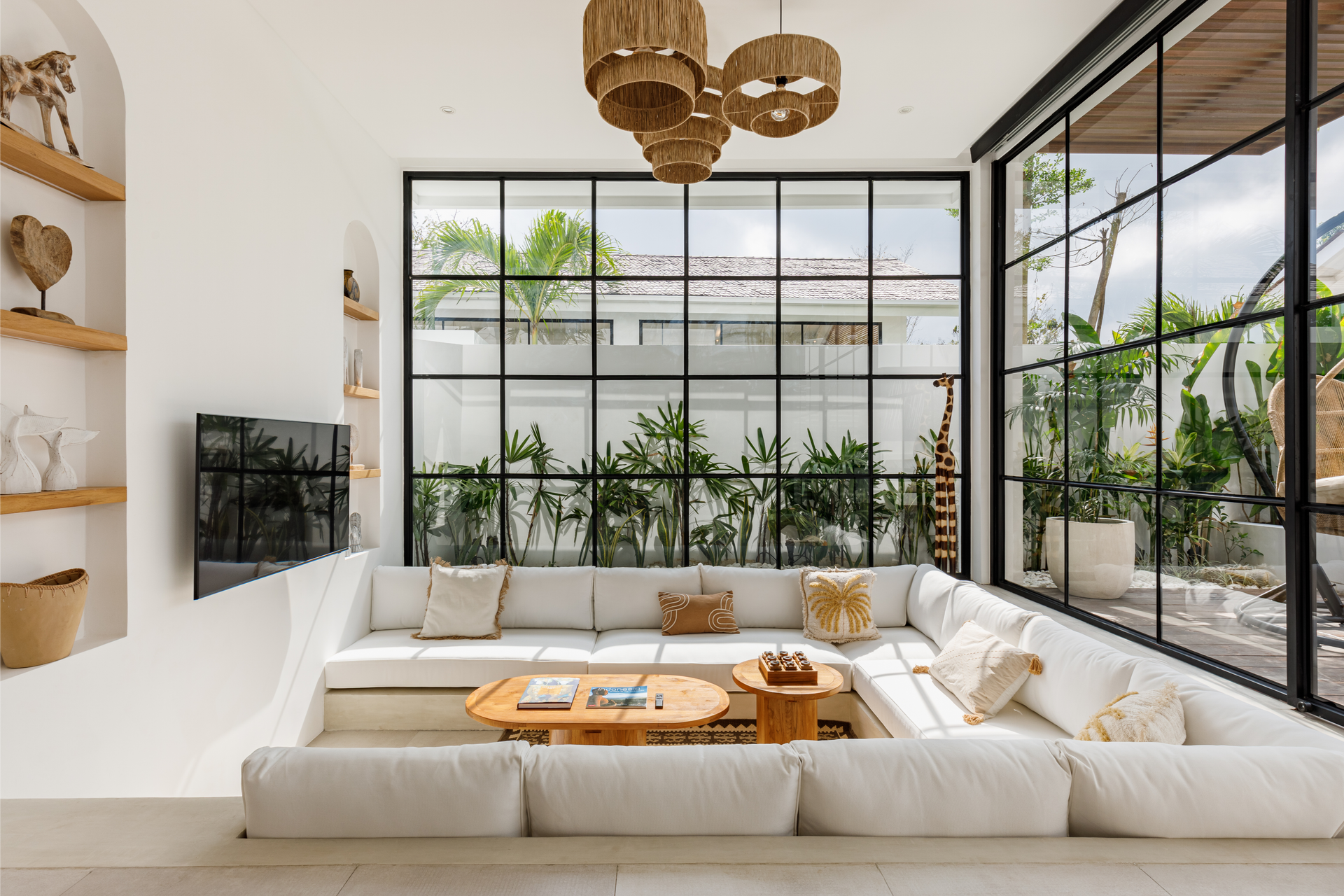 Bright modern living room with white sectional sofa, wood coffee table, and large black-framed windows overlooking greenery