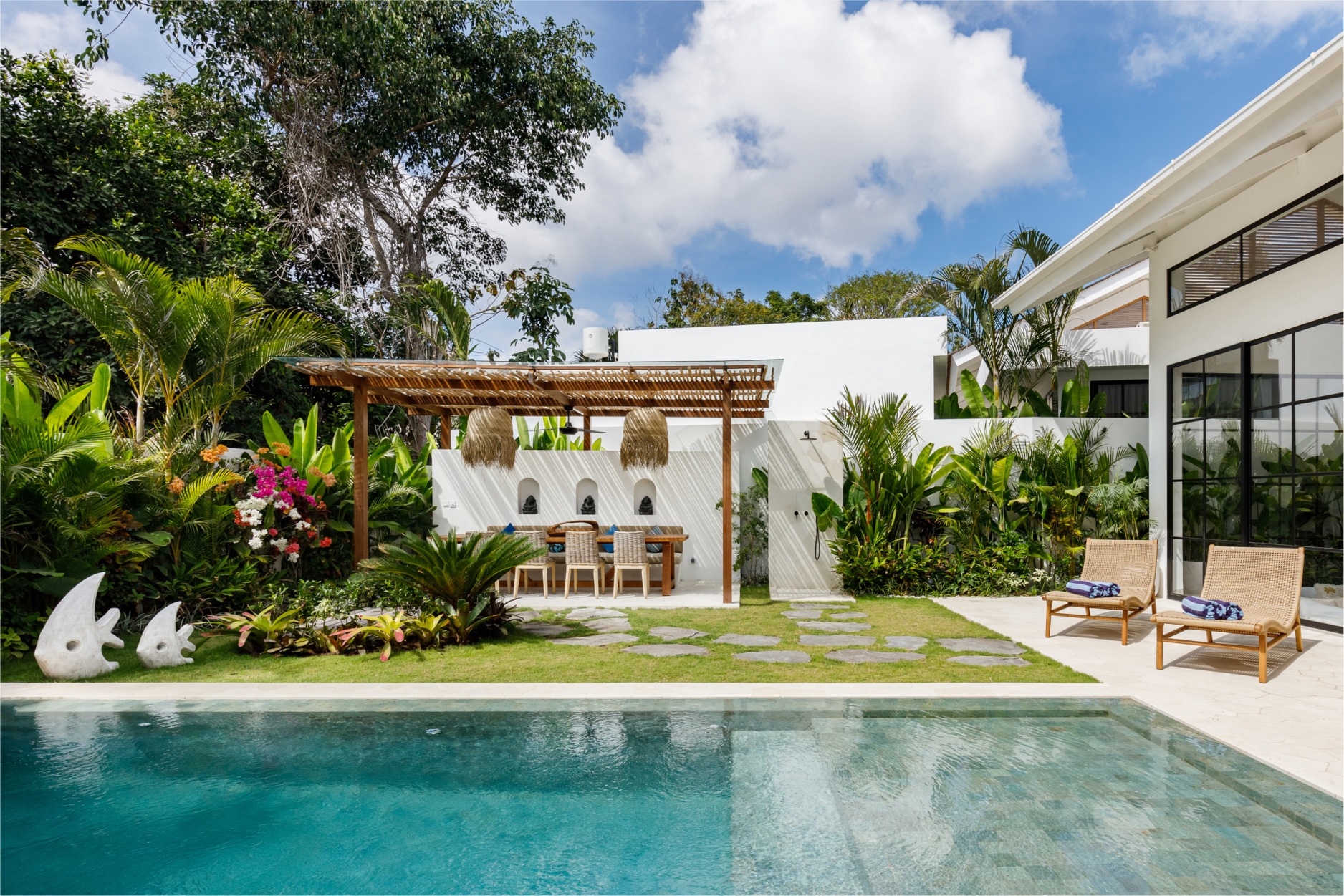Luxury tropical poolside villa with lounge chairs, lush greenery, and bright blue water