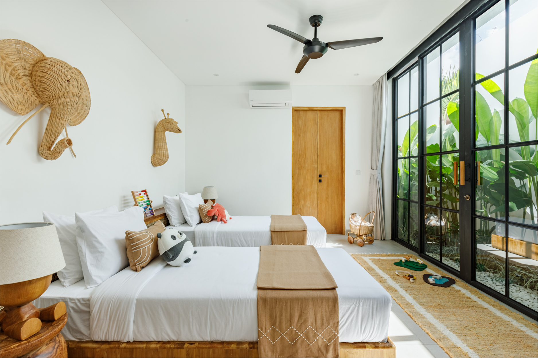Bright bedroom with twin beds, woven decor, black-framed windows, and a wooden door.