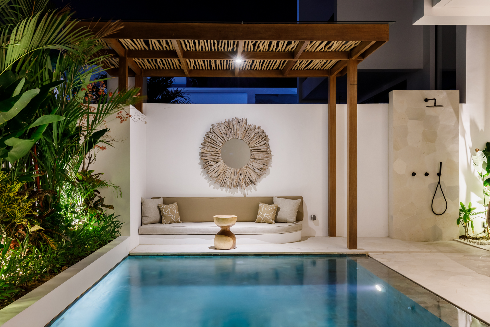 Modern poolside cabana with white seating, woven wall decor, and blue water at night