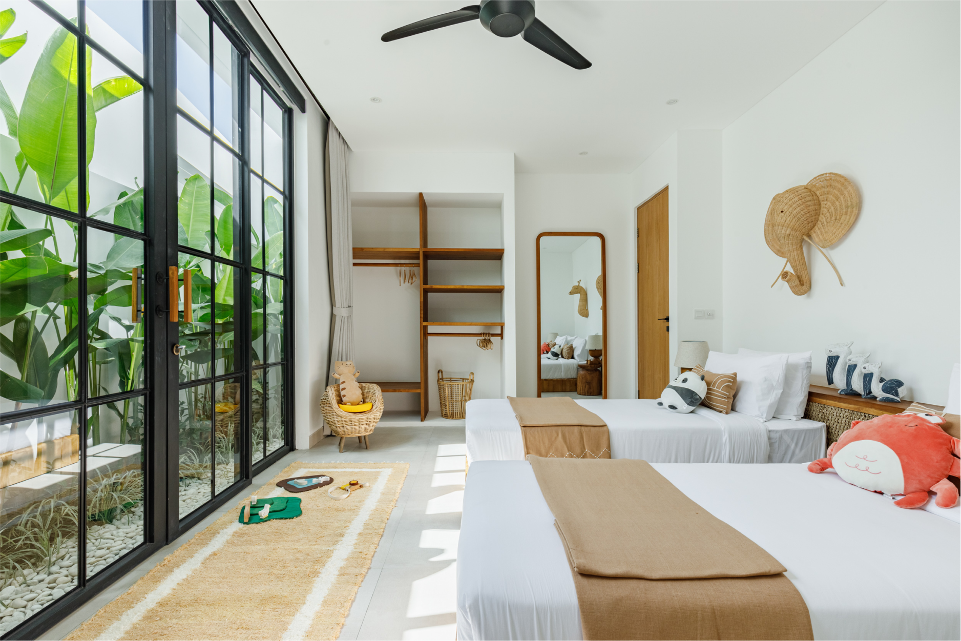 Bright bedroom with large windows, twin beds, wood shelves, and woven wall decor