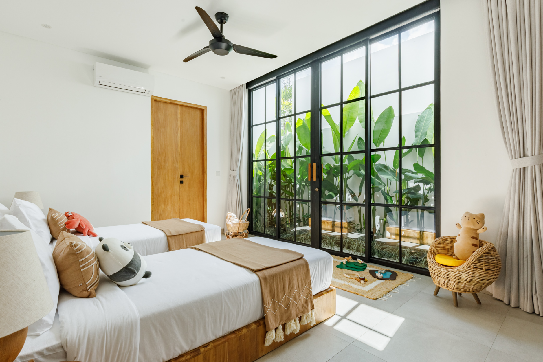 Bright bedroom with twin beds, large floor-to-ceiling windows, and tropical plants outside