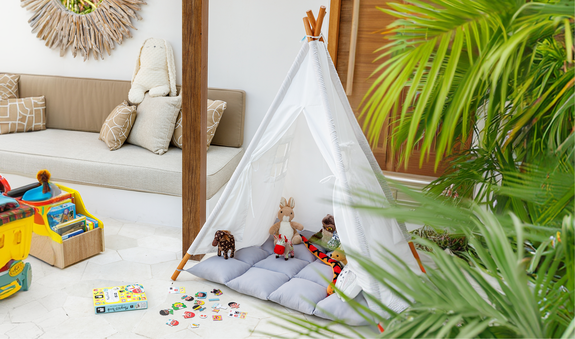 Children’s play tent with toys on a bright living room floor beside a beige sofa and tropical plant