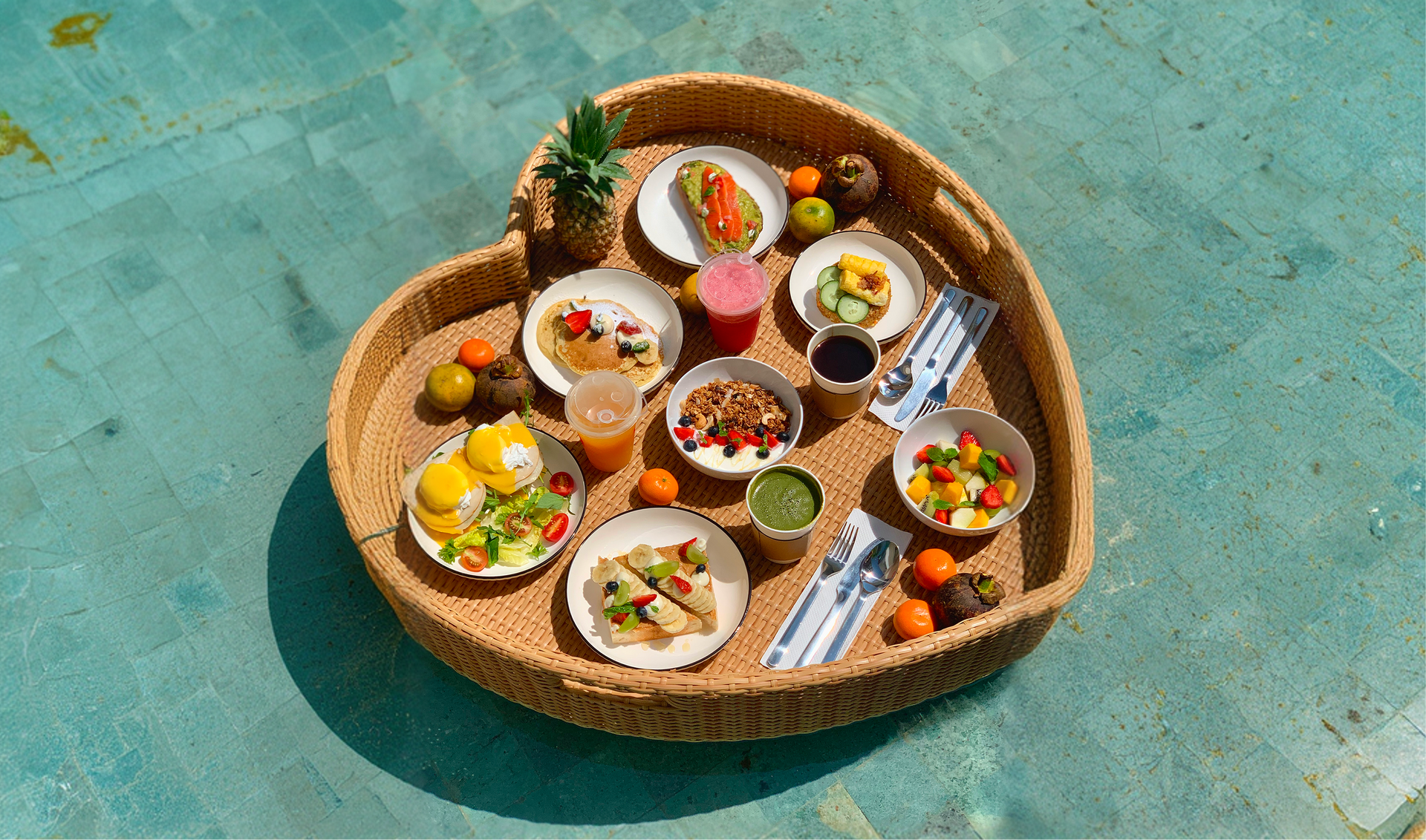 Round basket of assorted snacks and fruit bowls on a turquoise surface outdoors