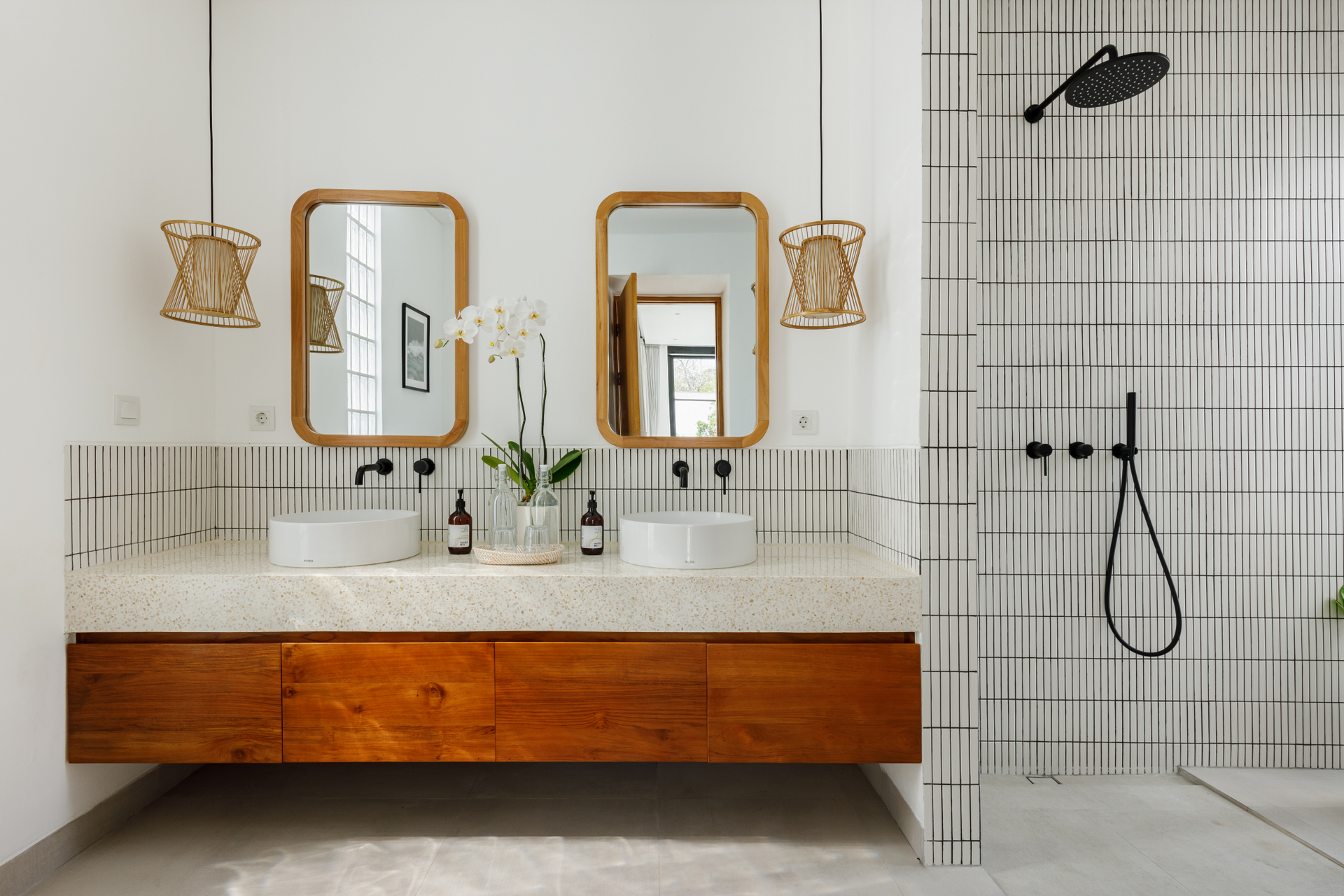 Modern bathroom with wood vanity, two mirrors, and tiled shower with black fixtures
