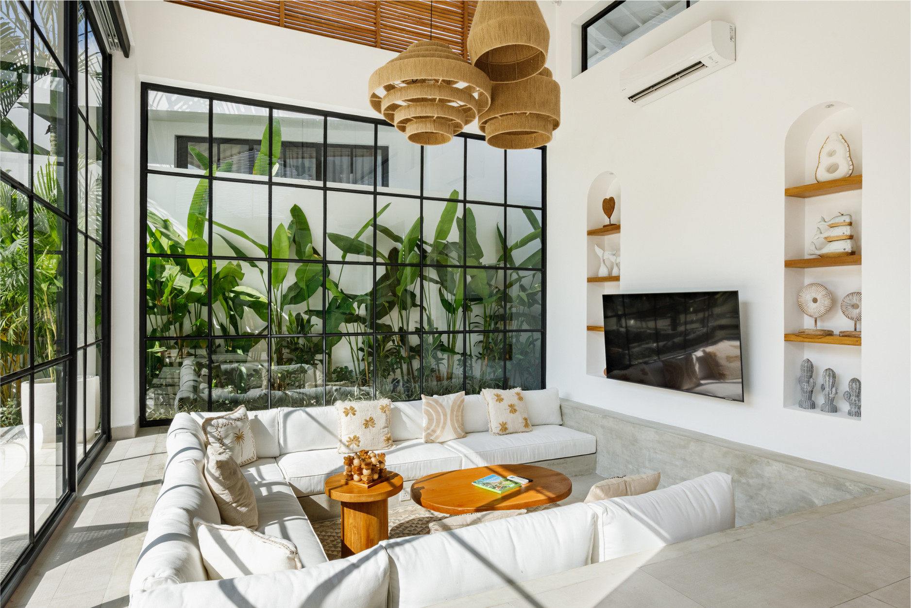 Bright modern living room with white sofas, indoor plants, black-framed windows, and wicker pendant lights