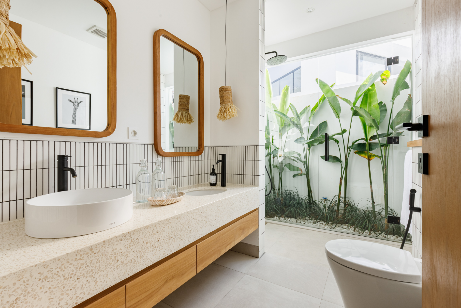 Bright modern bathroom with double vanity, round mirror, wood accents, and tropical shower partition
