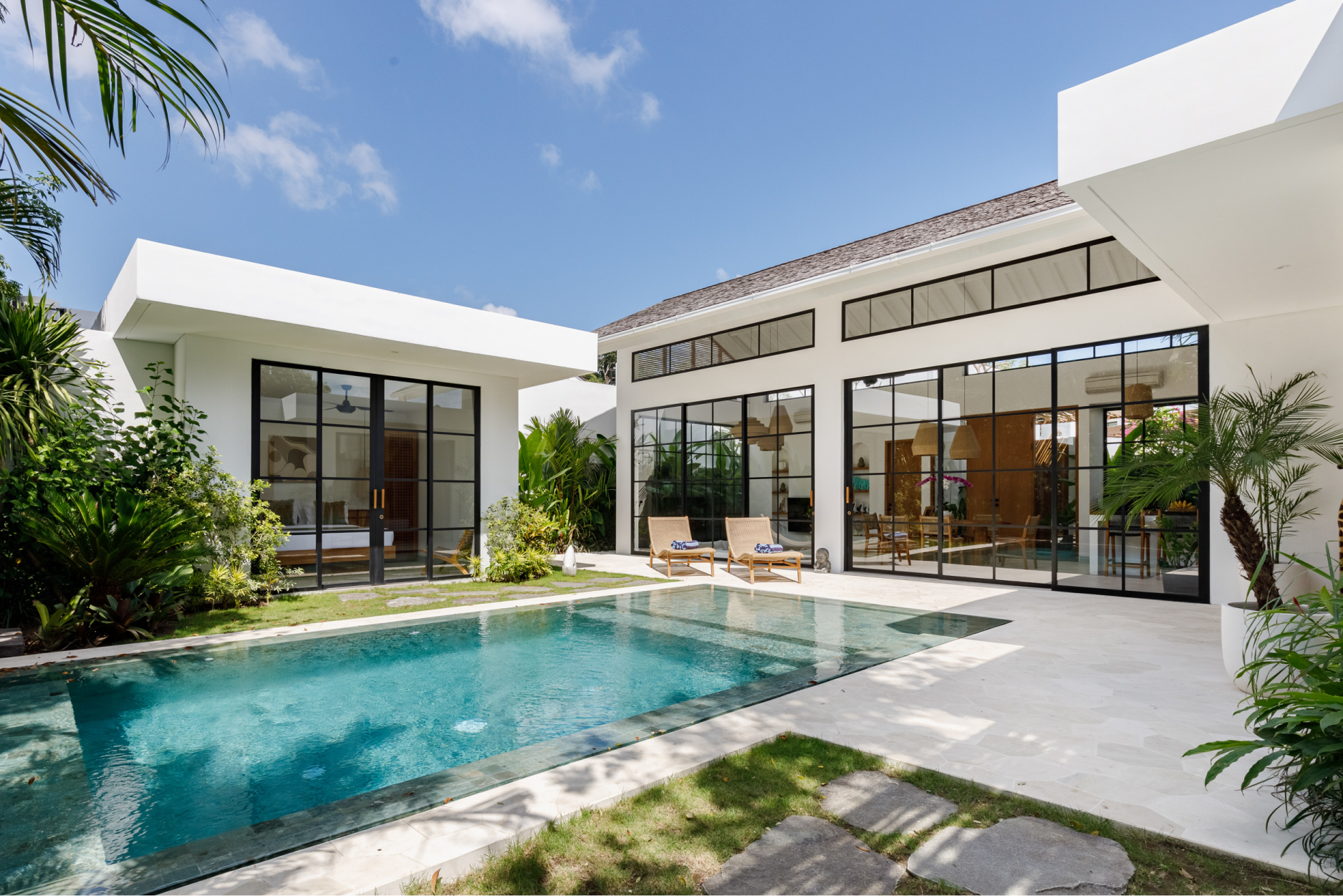 Modern white villa with a turquoise pool and sunlit patio under a clear blue sky