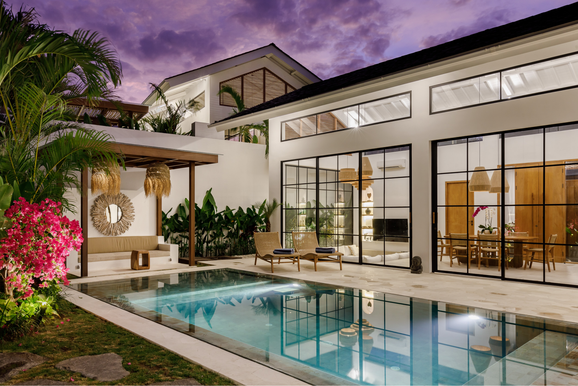 Modern villa courtyard with a pool, palm trees, and warm-lit patio at dusk