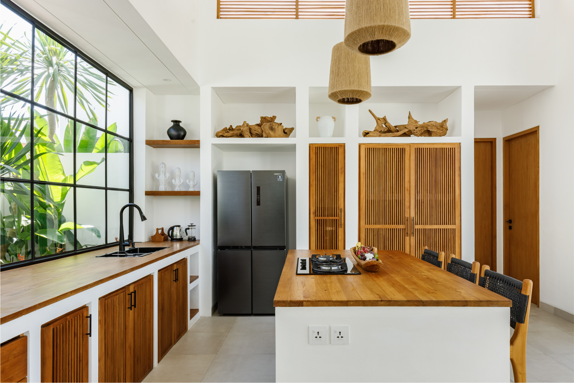 Bright modern kitchen with wood cabinets, white counters, black fridge, and large window.