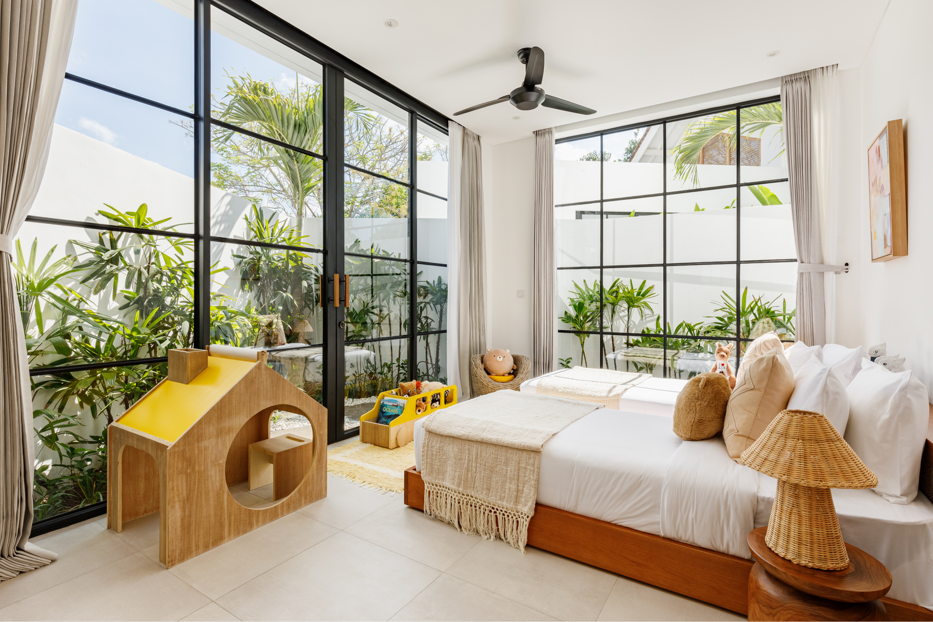 Bright modern bedroom with large windows, white bed, and a small wooden playhouse by plants