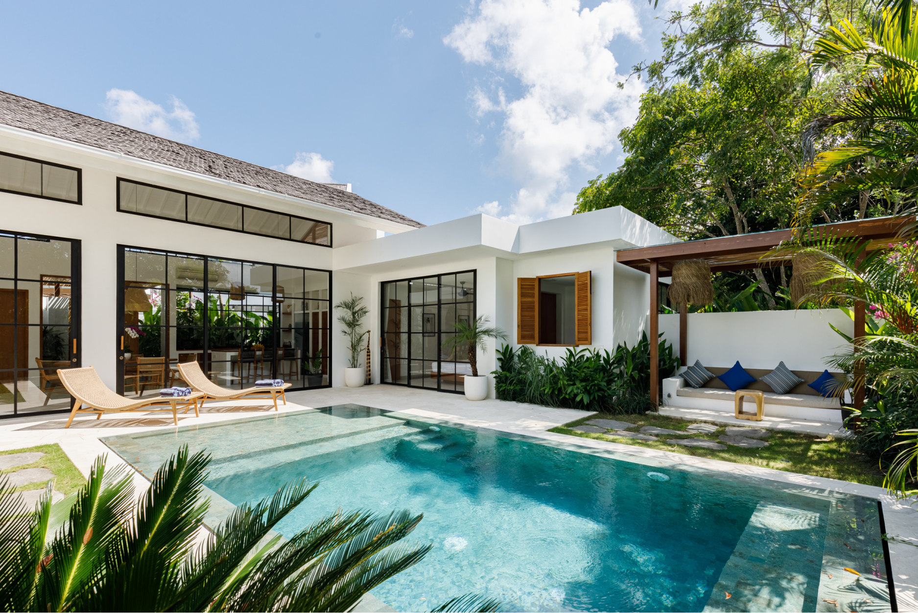 Modern backyard patio with a turquoise pool, loungers, and a house with large glass doors