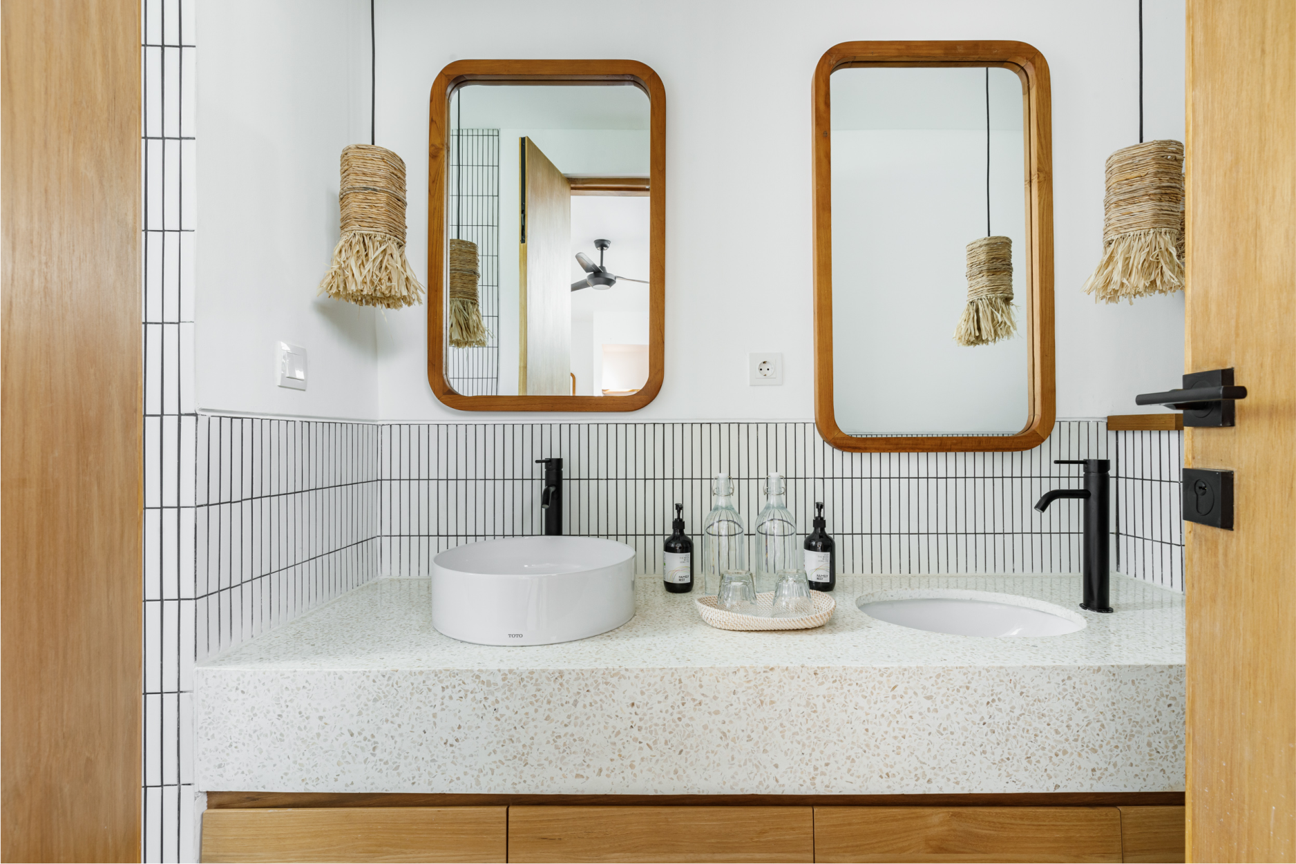 Modern bathroom vanity with round sink, gold-framed mirrors, white tile, and woven pendant lights