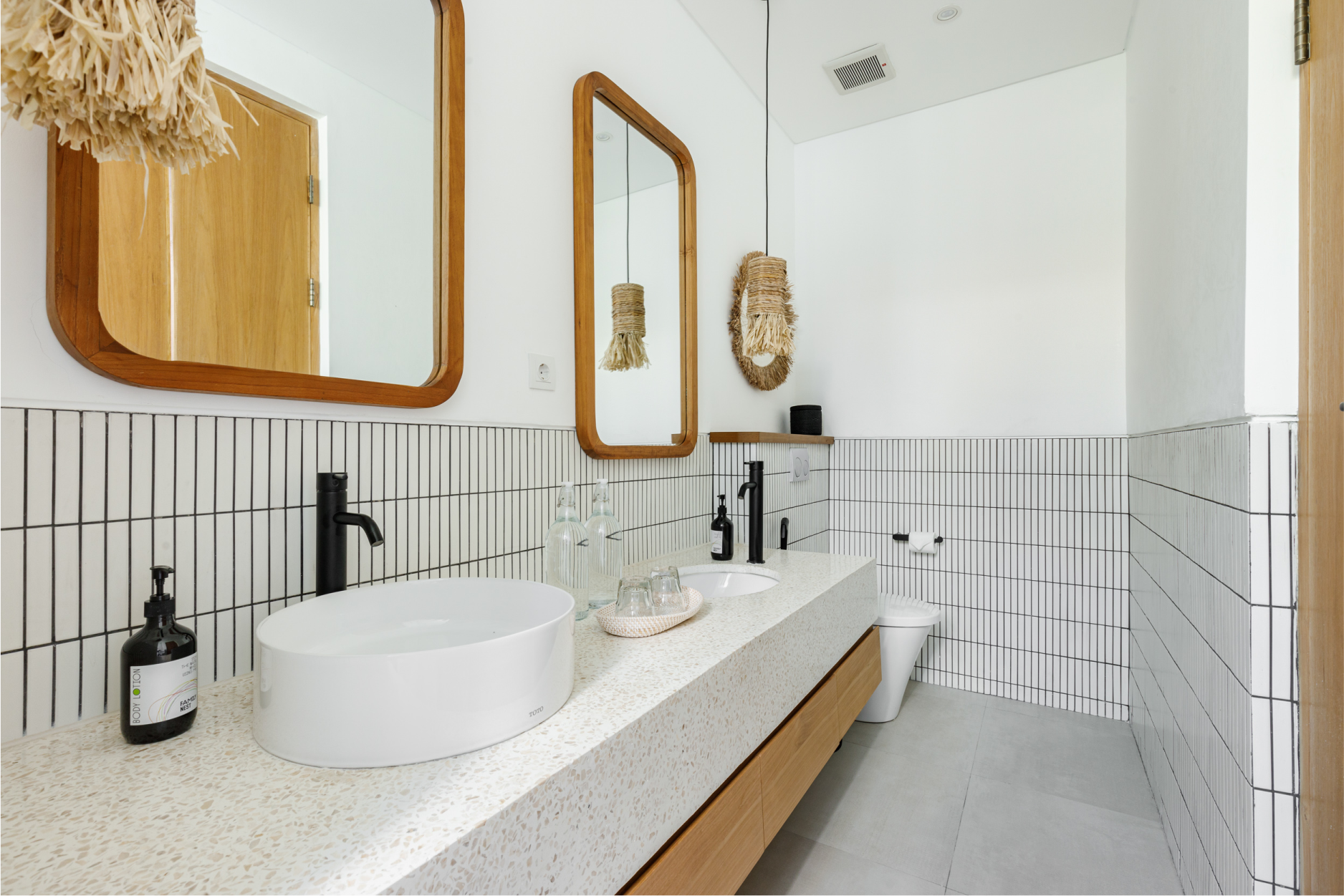 Modern bathroom with white double sink vanity, wood-framed mirrors, and tiled walls