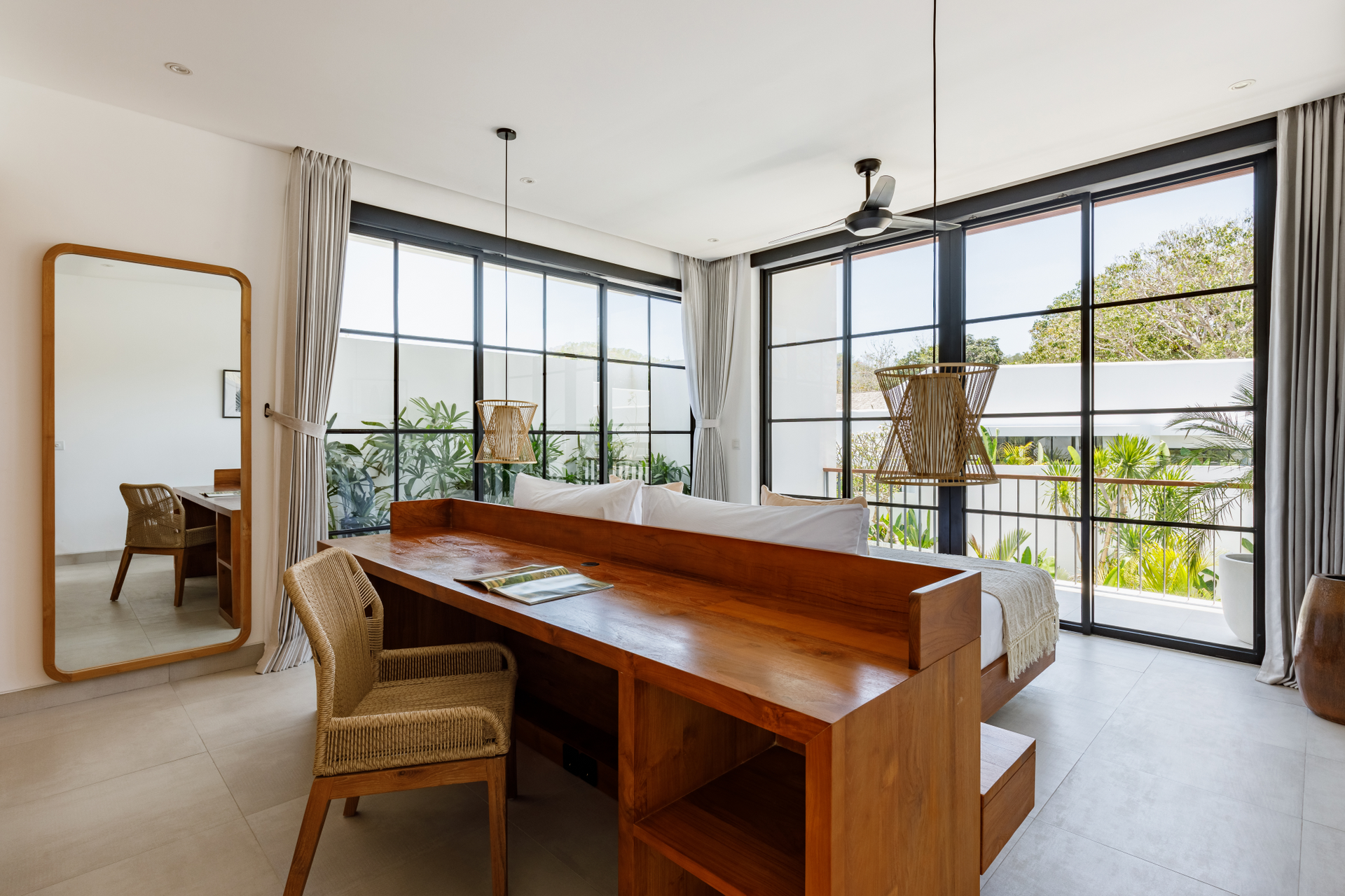 Bright living room with a wooden desk, woven chair, large windows, and a balcony view.