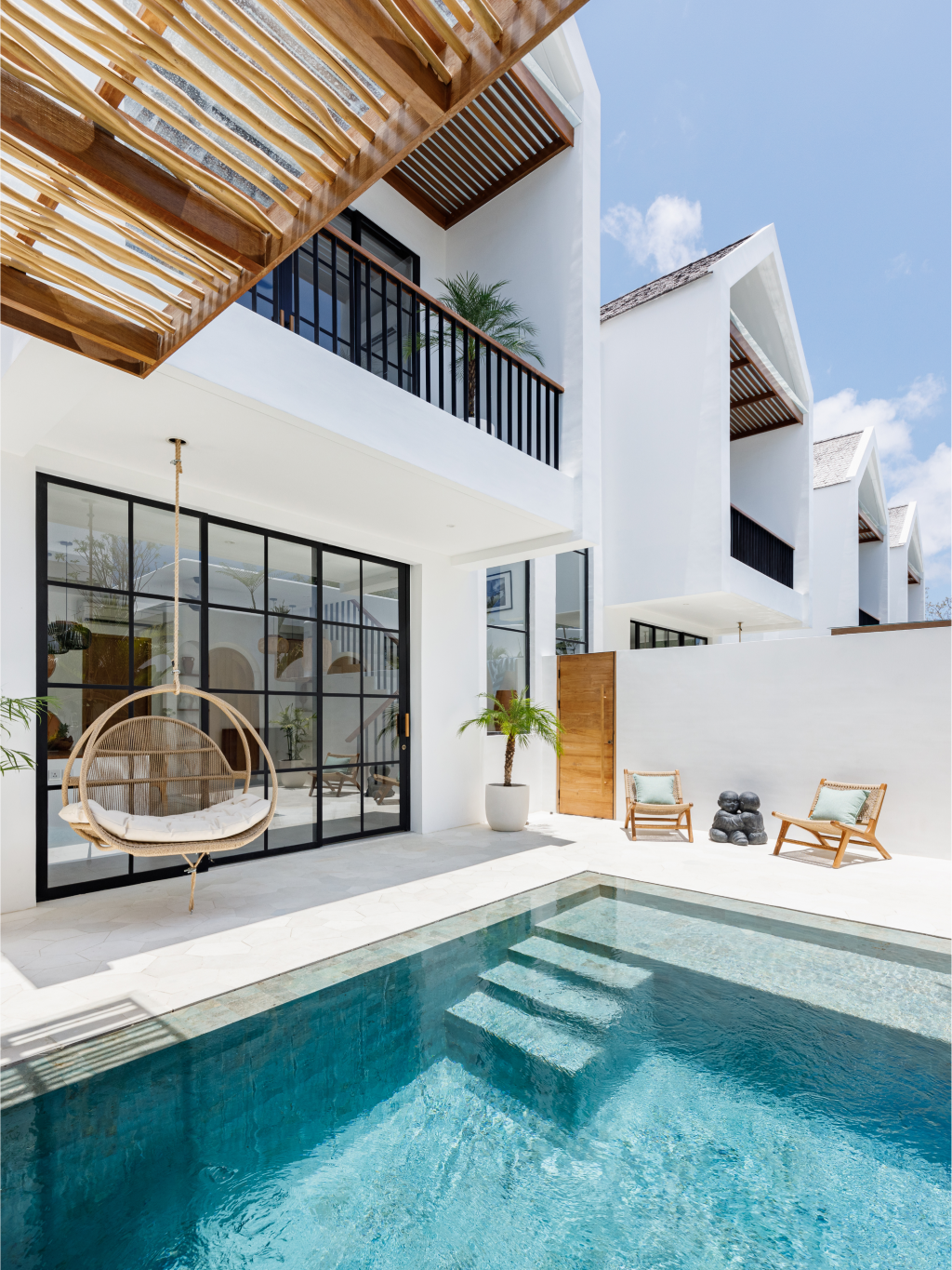 Modern white villa courtyard with a turquoise pool, hanging chair, and shaded balcony