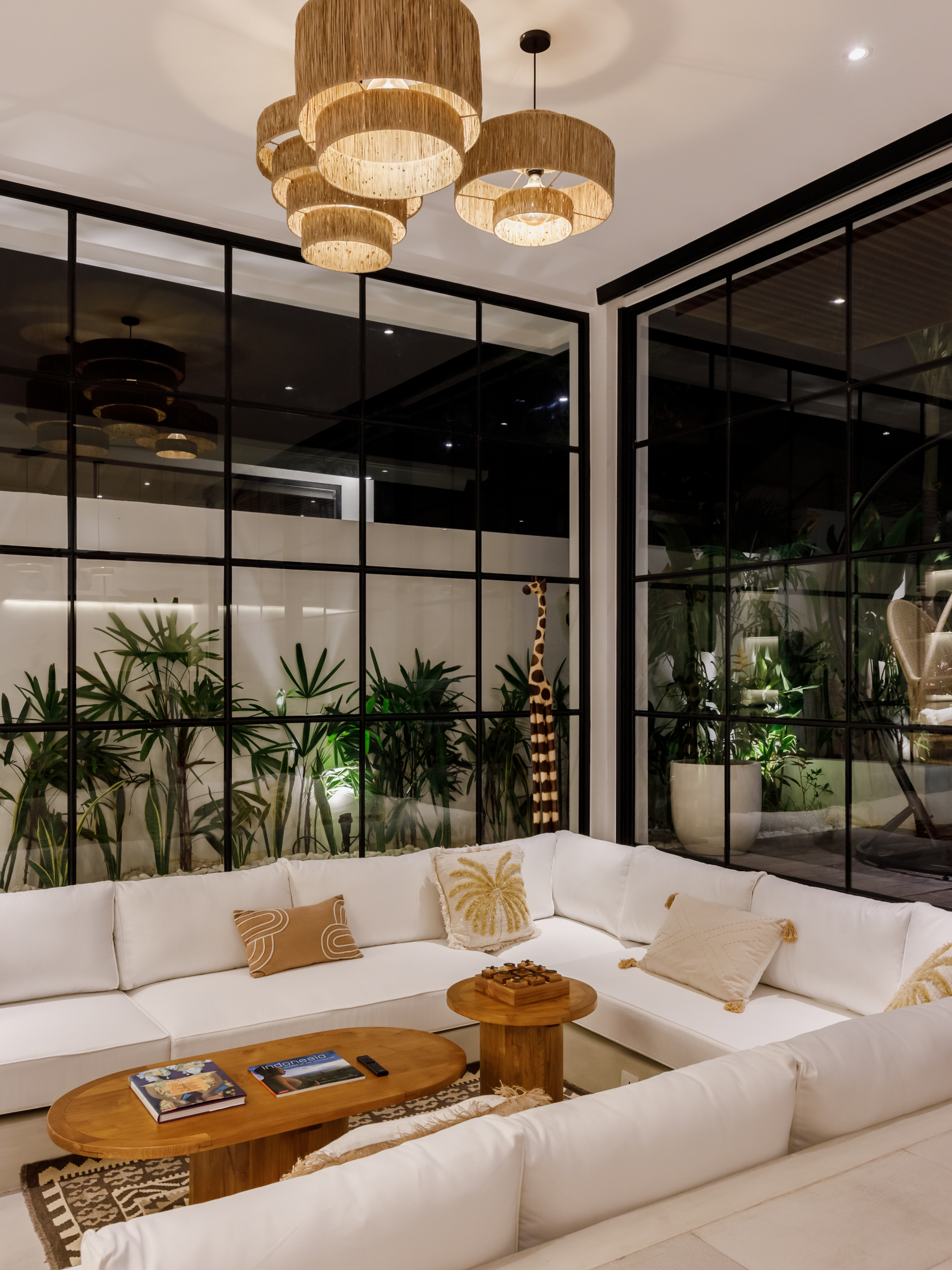 Elegant modern living room with white sectional sofa, wooden coffee table, and gold pendant lights in a glass-walled space