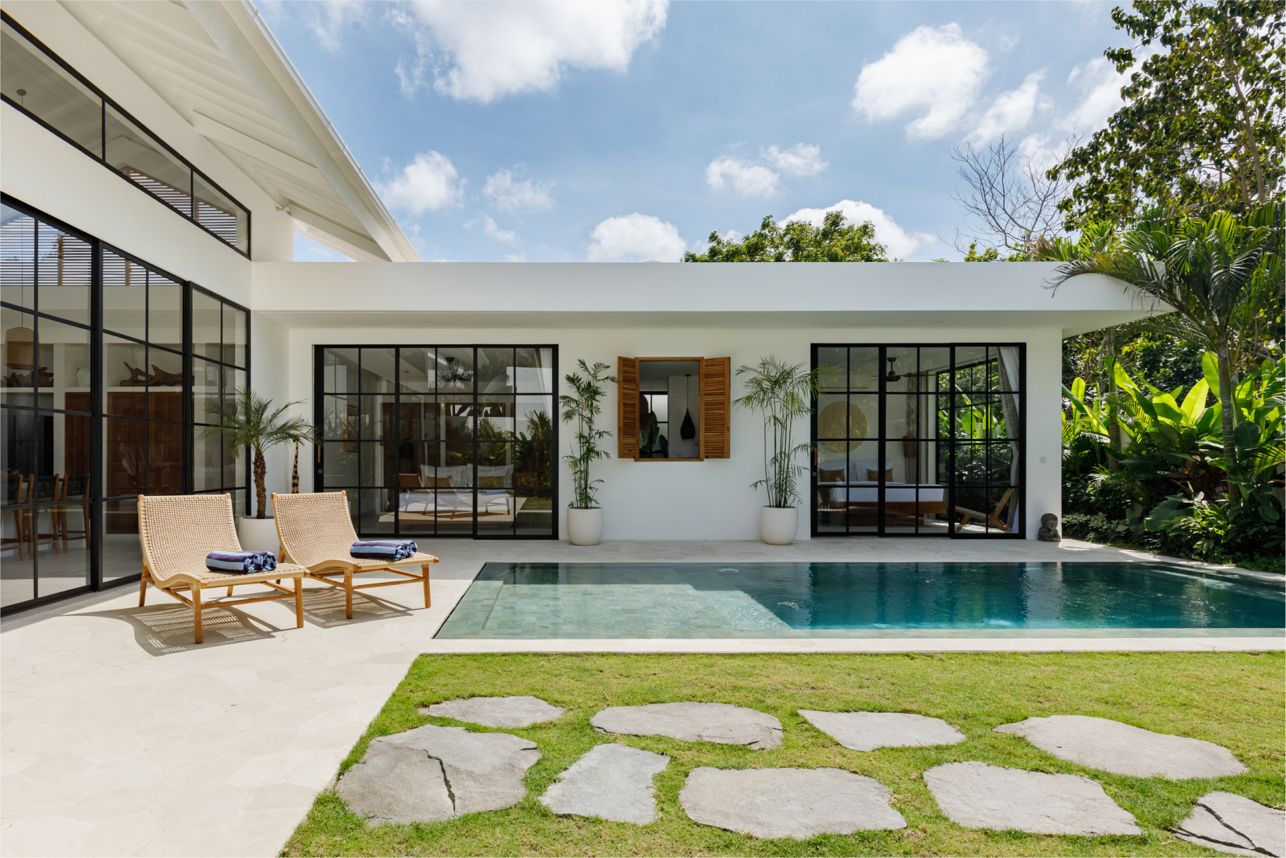 Modern white house with glass doors, patio chairs, pool, and lawn with stepping stones
