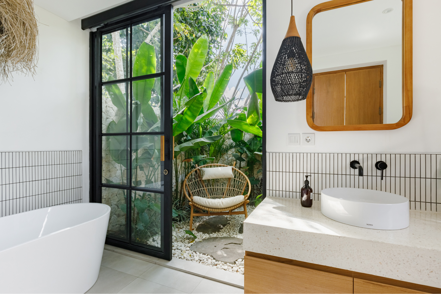 Modern bathroom with freestanding tub, black-framed door to greenery, and vanity with round mirror