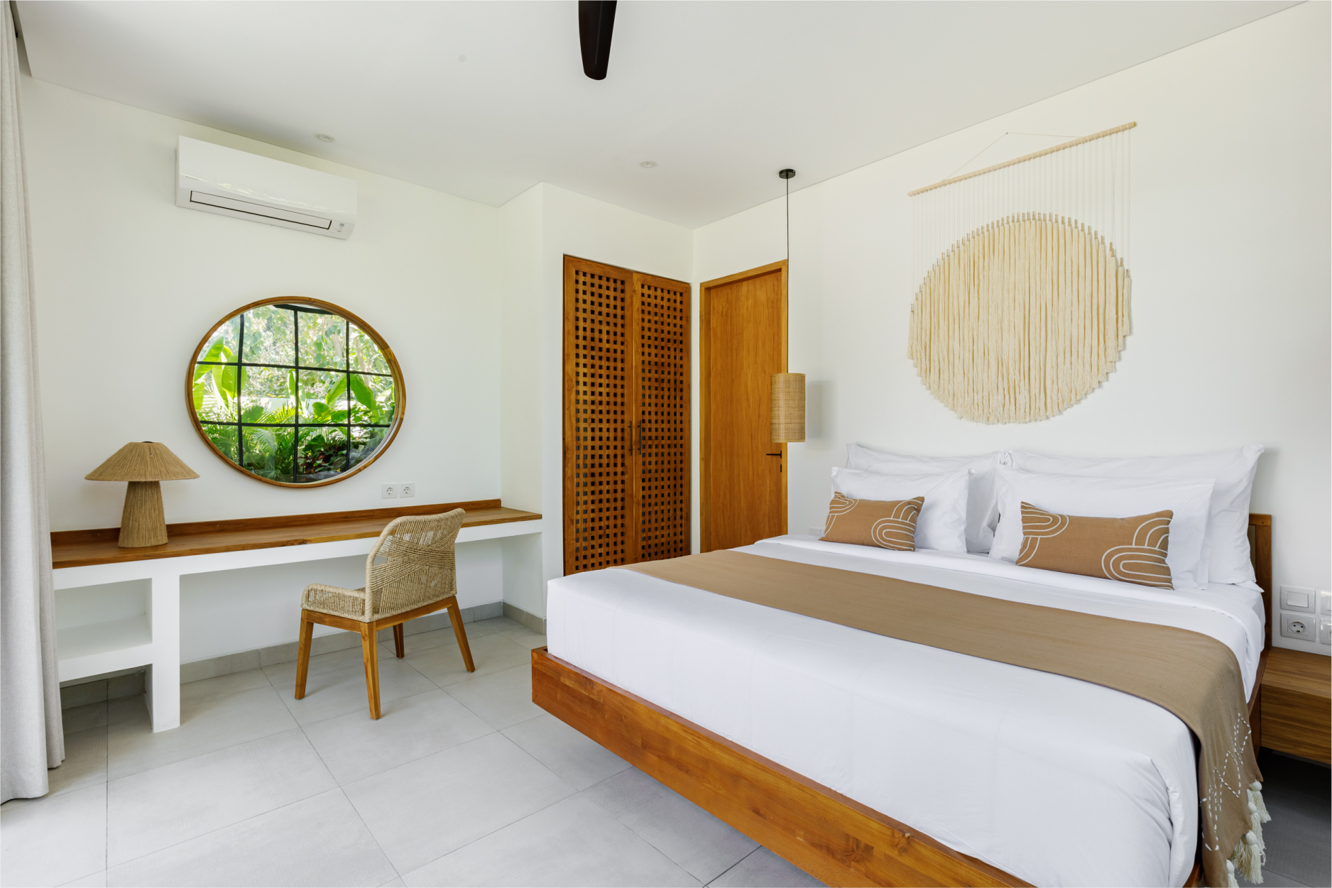 Bright minimalist bedroom with a wooden bed, desk, chair, round mirror, and woven decor