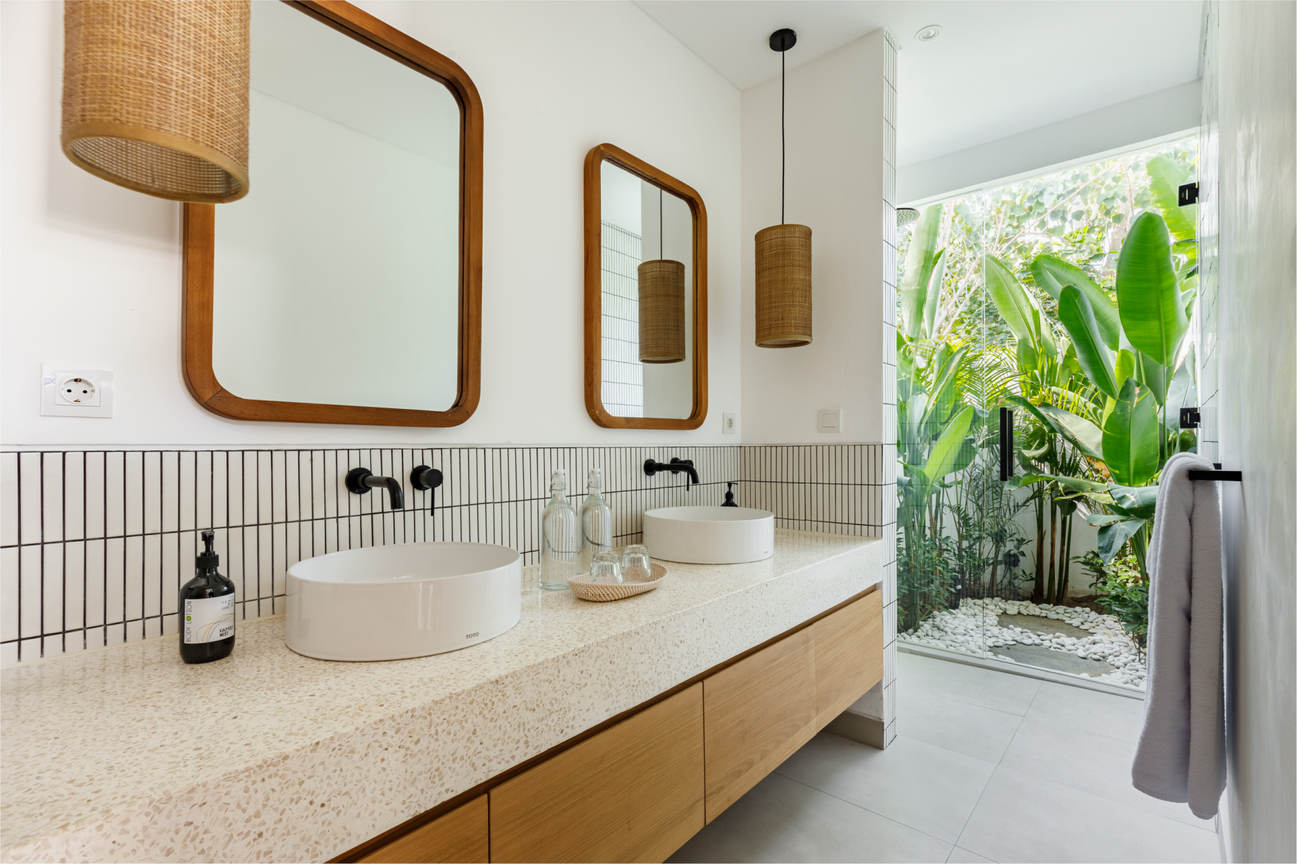 Modern bathroom vanity with round mirrors, woven pendant lights, and a view of lush greenery outside.
