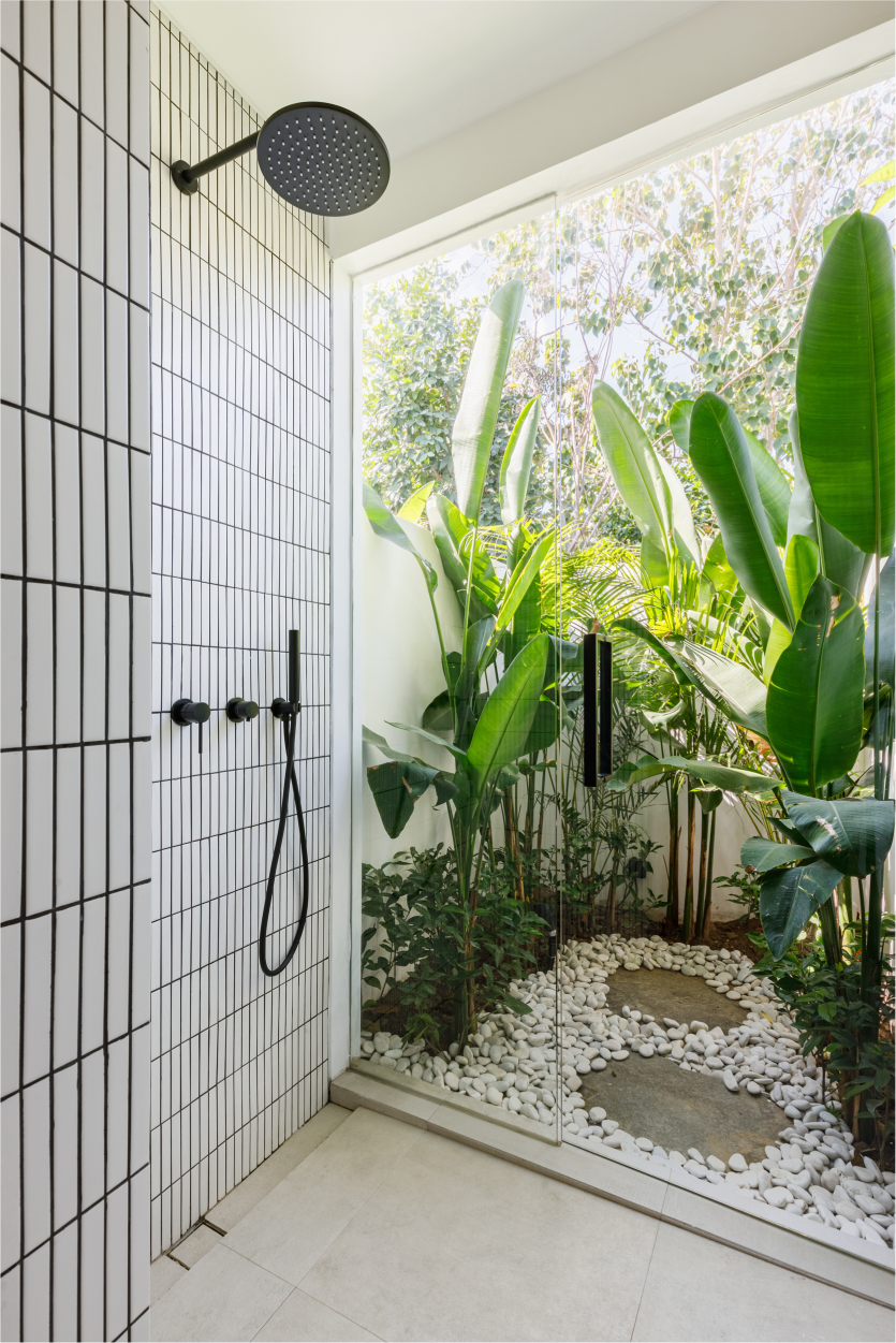 Outdoor shower with black tile walls, black fixtures, and lush tropical plants and pebbles nearby