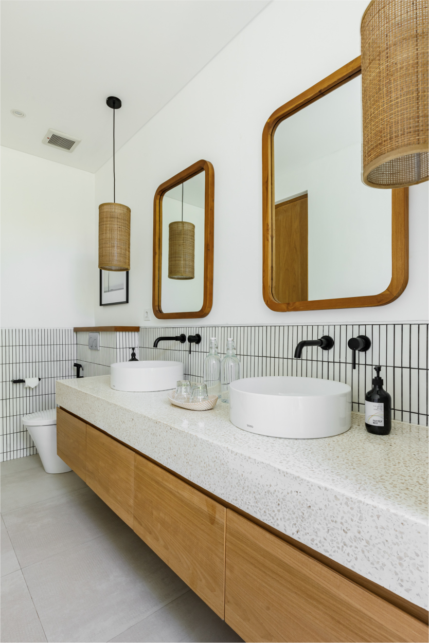 Modern bathroom vanity with wood cabinets, speckled countertop, round sinks, and woven pendant lights