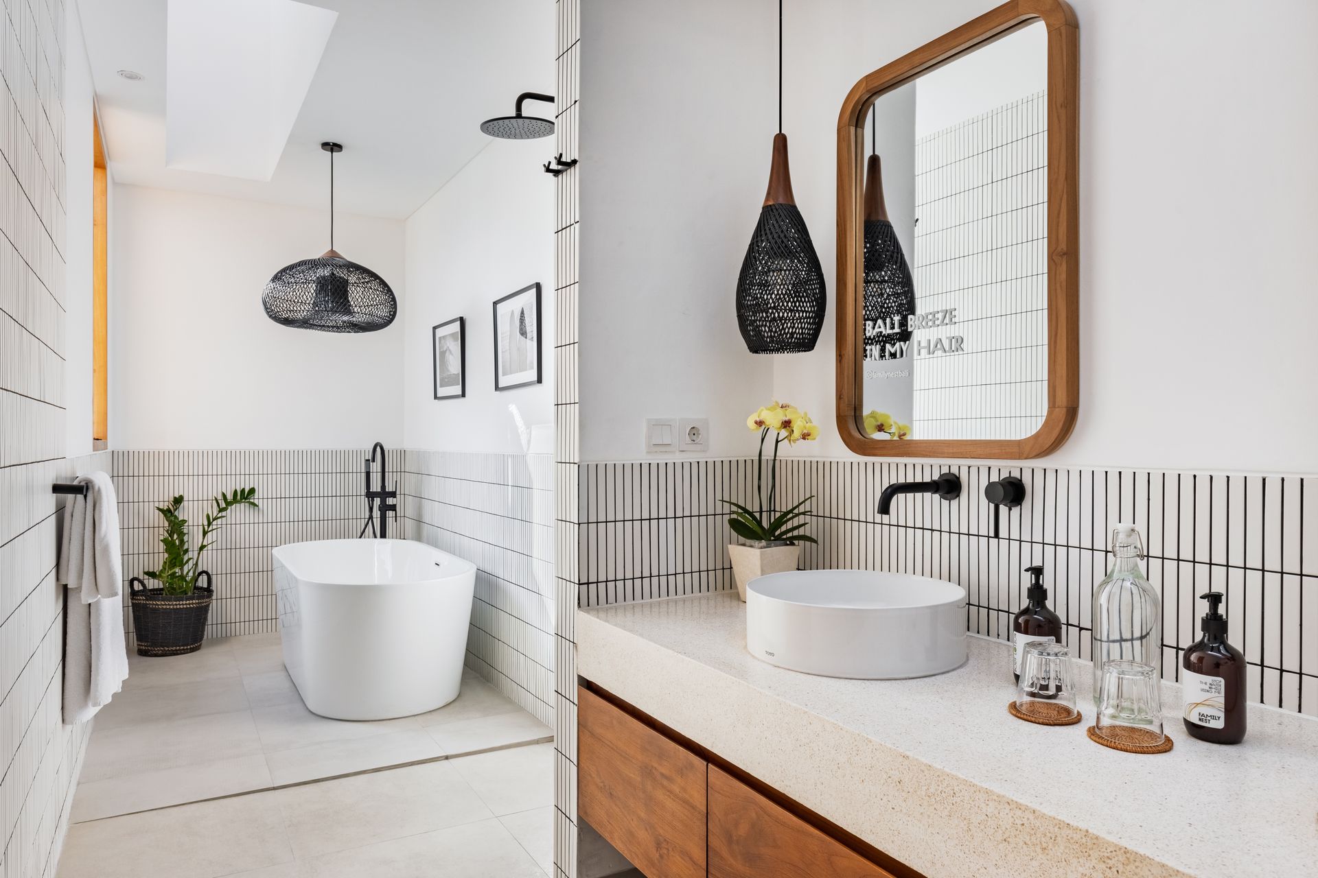 Bright modern bathroom with white tub, vanity, tiled walls, and hanging black pendant light