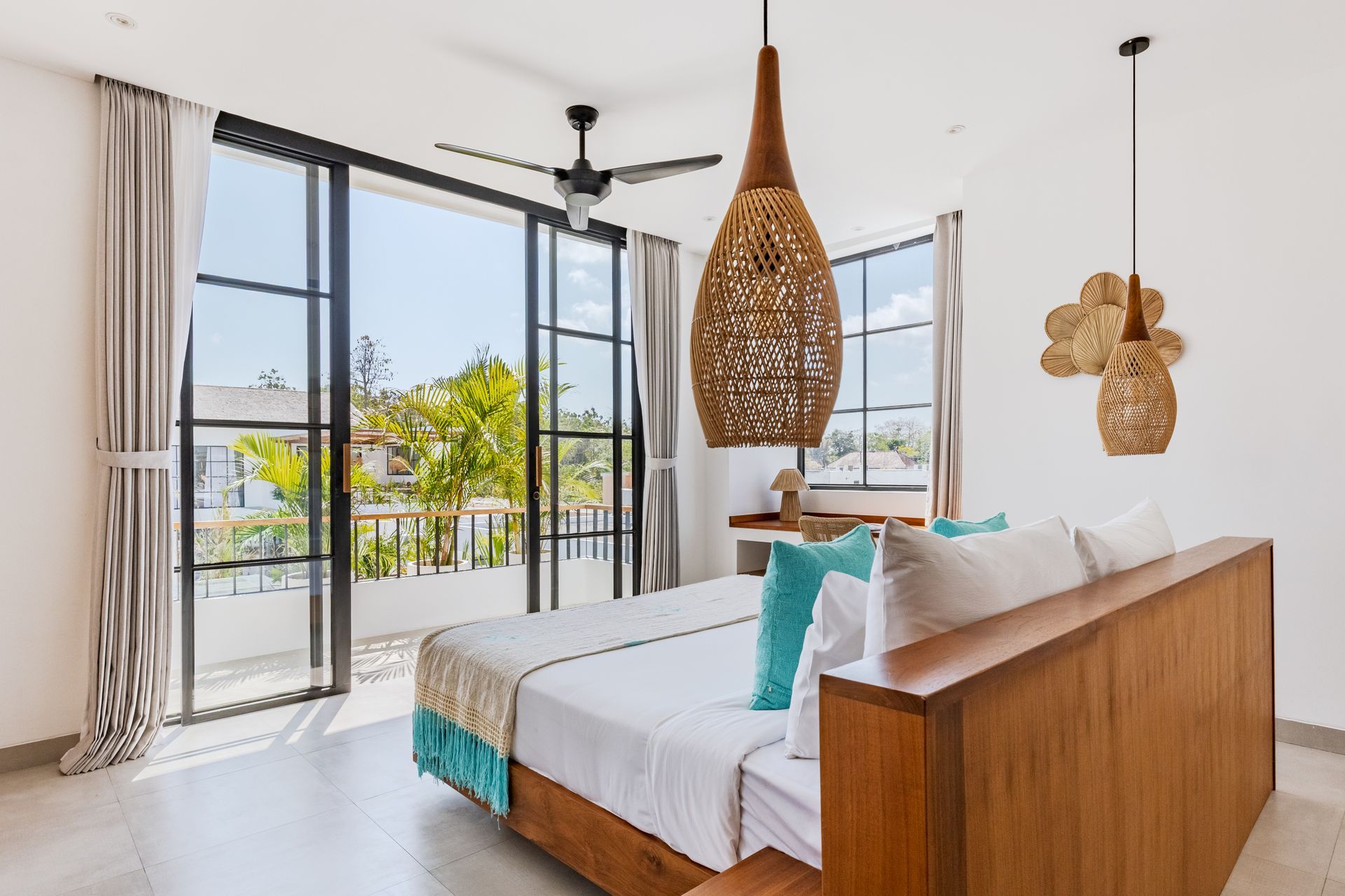 Bright beachfront bedroom with wooden bed, woven pendant lights, and open balcony doors