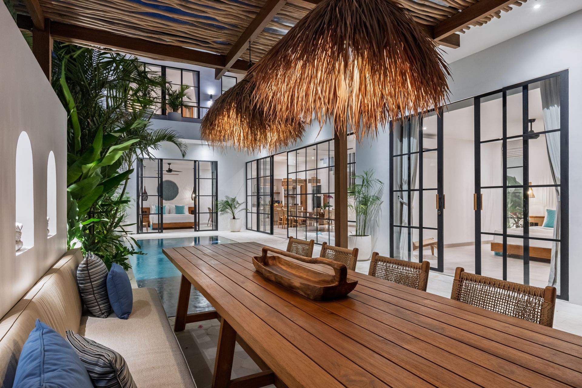 Spacious tropical dining room with wooden table, woven chairs, and large glass doors opening to a patio