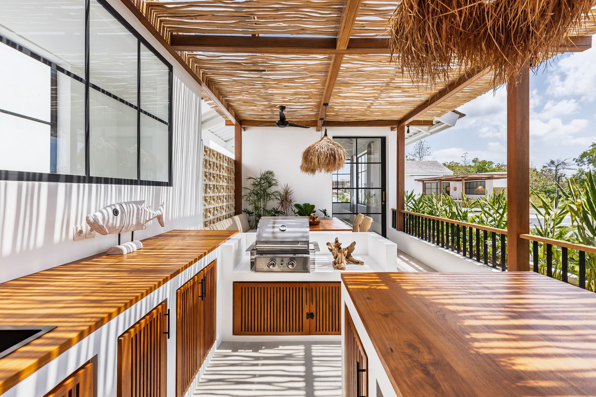 Open-air wooden kitchen with white countertops, woven pendant lights, and tropical balcony view