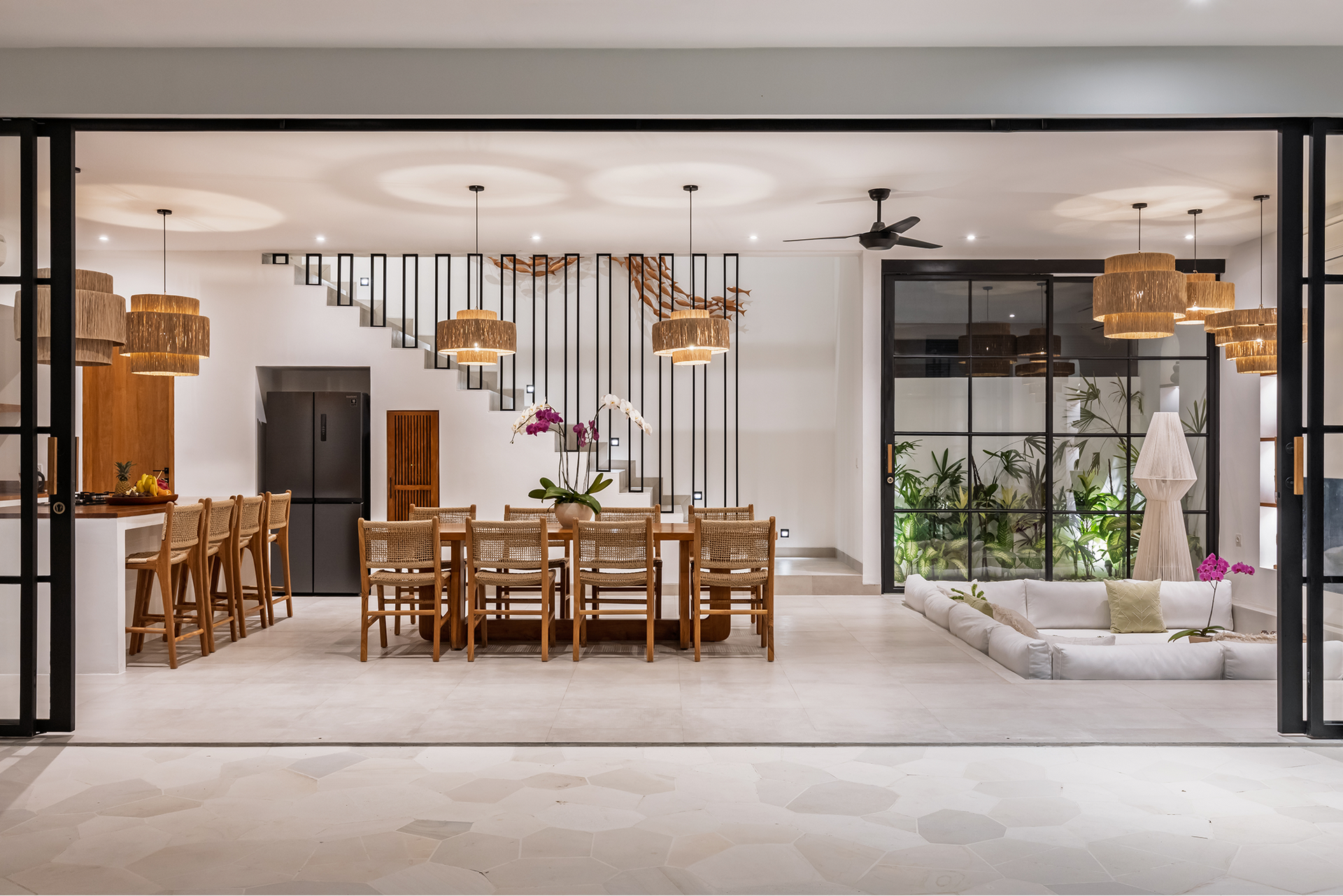 Modern open-plan dining and living room with wood table, pendant lights, and indoor plants