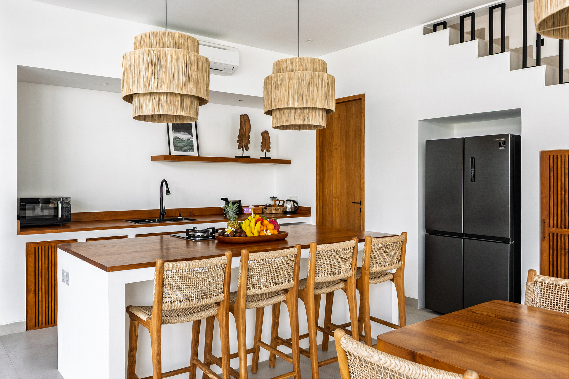 Modern kitchen with wood accents, woven pendant lights, island seating, and a black refrigerator