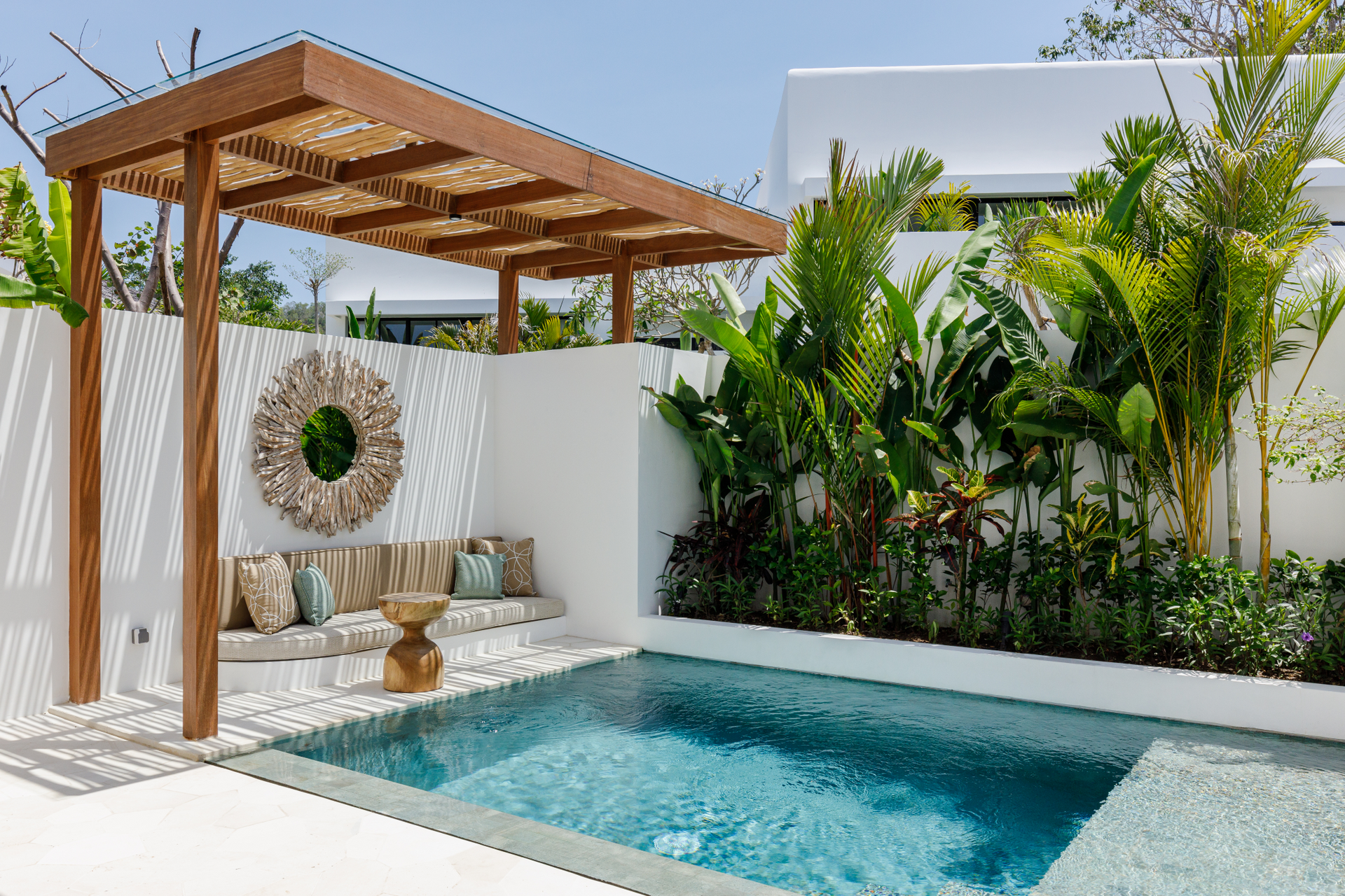 Modern backyard patio with a small pool, wooden pergola, built-in bench, and tropical greenery
