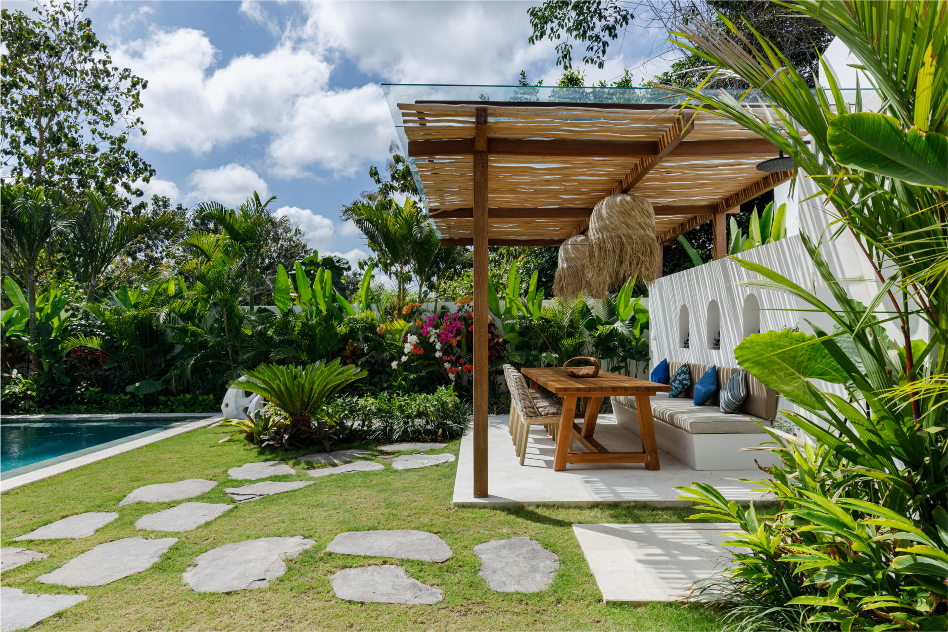 Tropical garden patio with wooden pergola, seating area, pool, and stepping stones on lawn