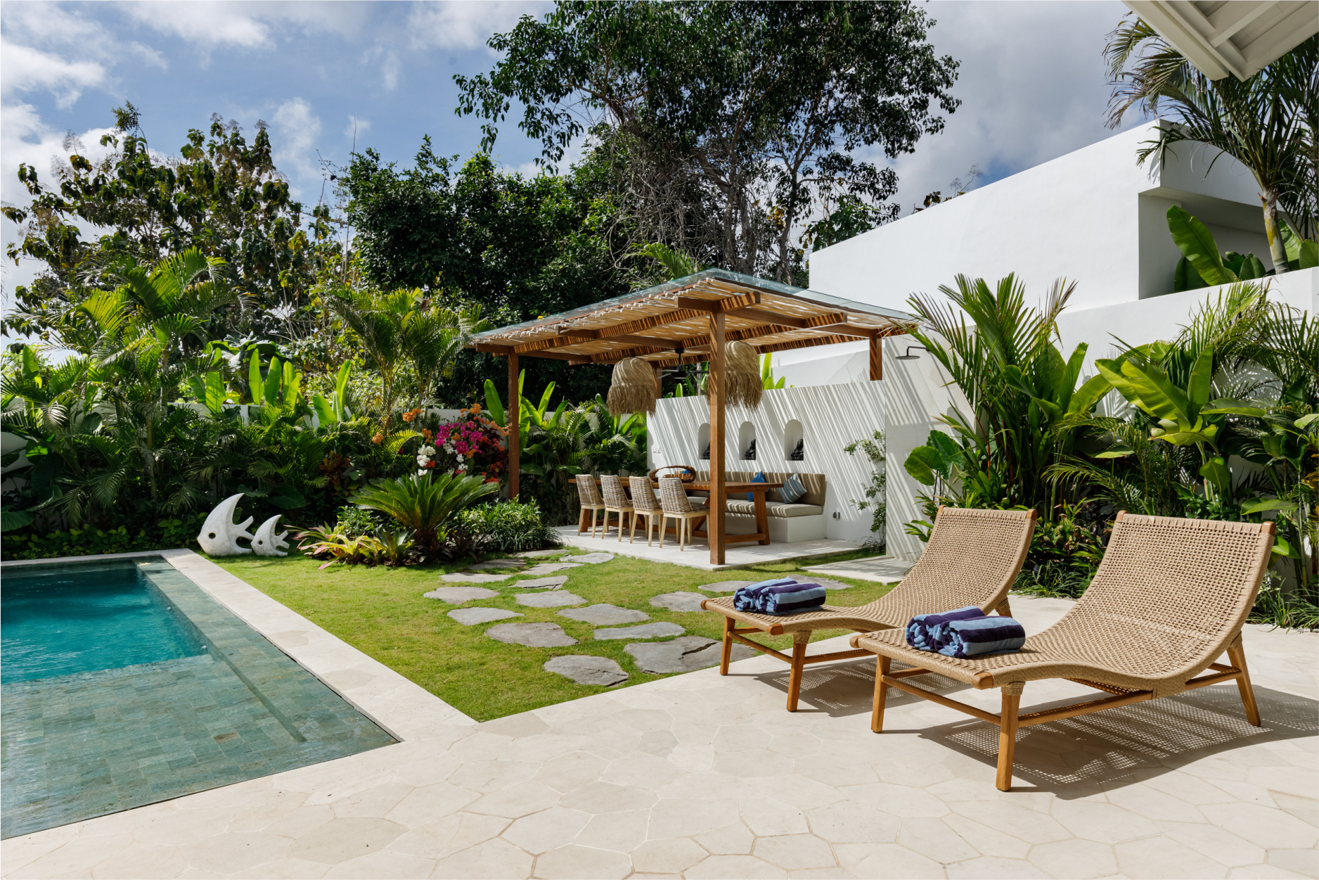 Modern backyard patio with pool, lounge chairs, shaded cabana, and lush tropical landscaping