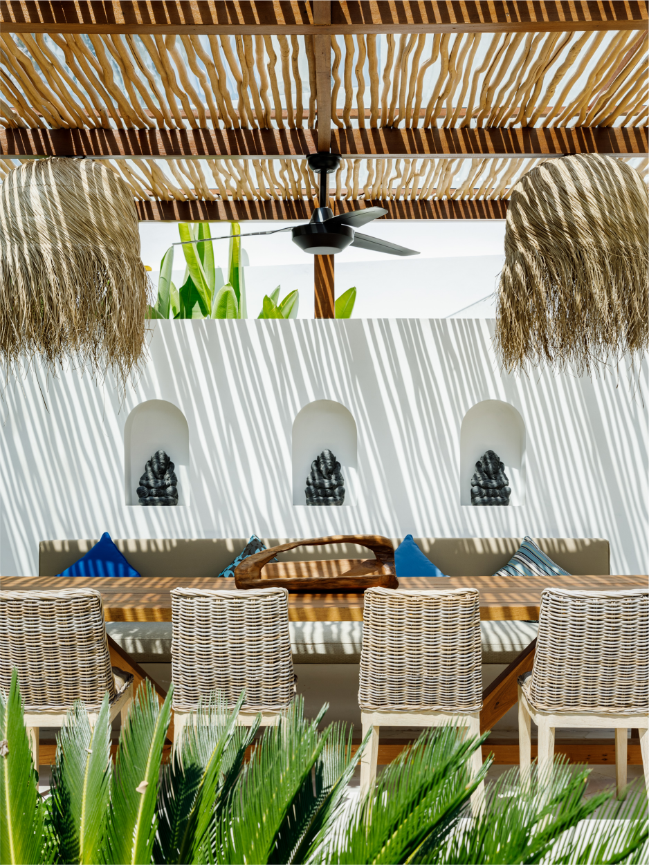 Beachfront lounge with wicker chairs, straw shade, white wall, and green plants