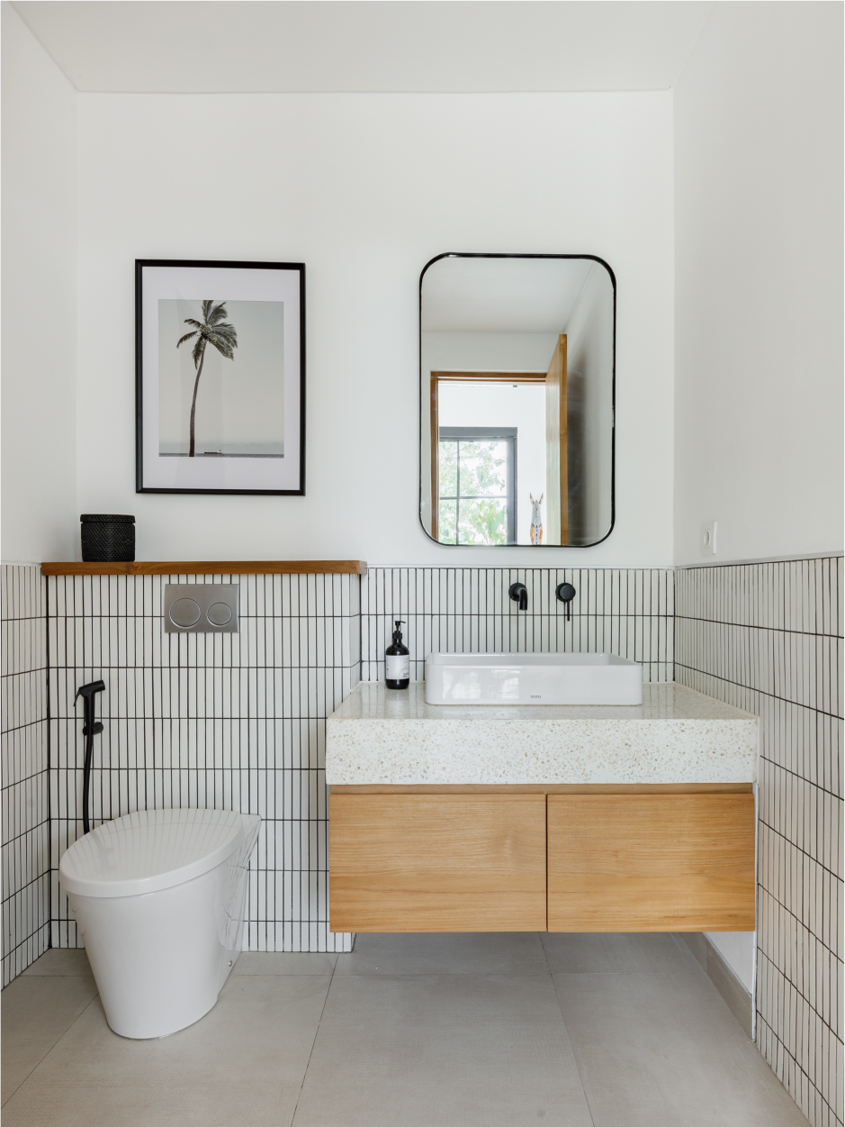 Minimalist bathroom with white tiled walls, wood vanity, round mirror, and framed palm print.