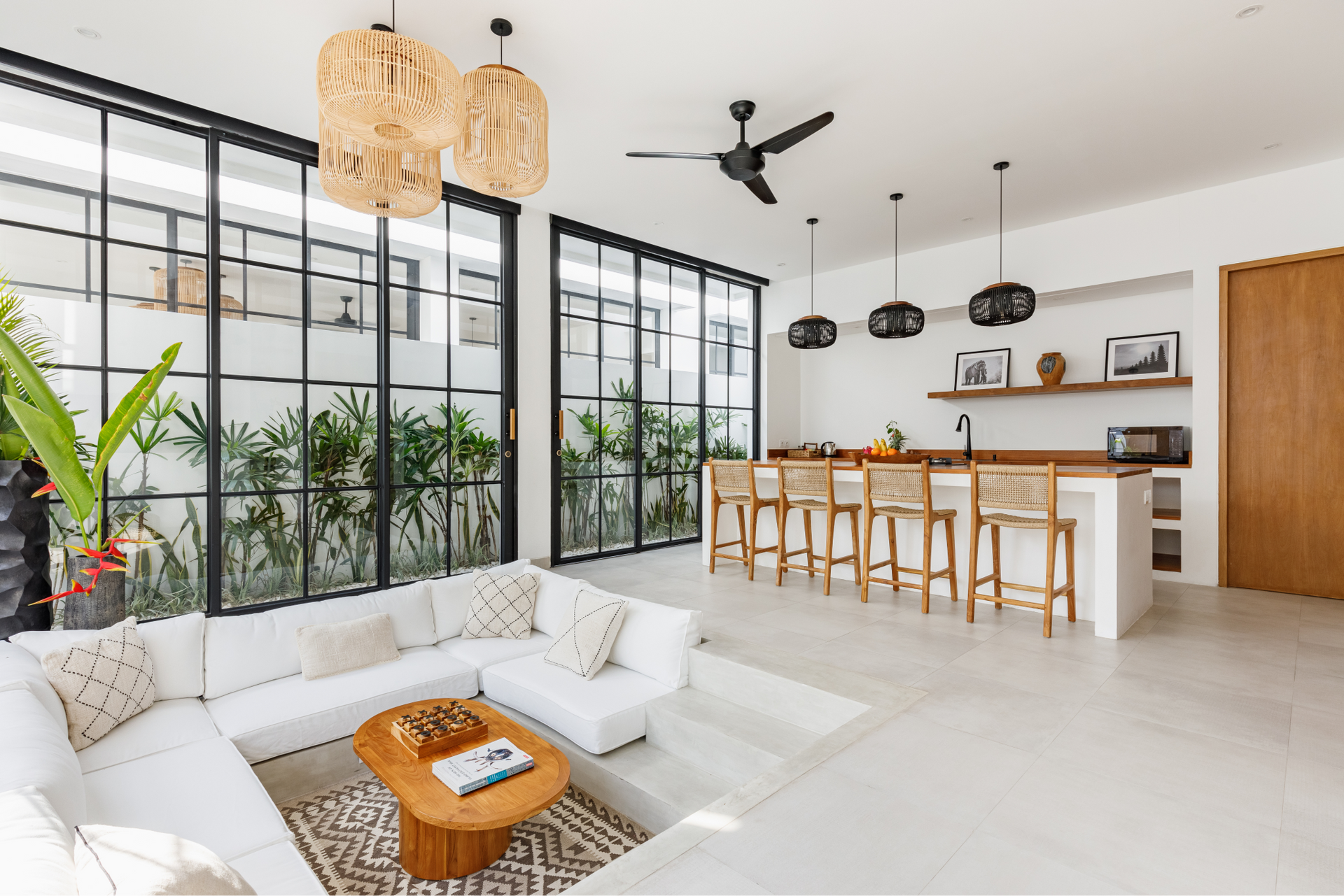 Bright open living room and kitchen with white sofa, wooden island, large windows, and plants